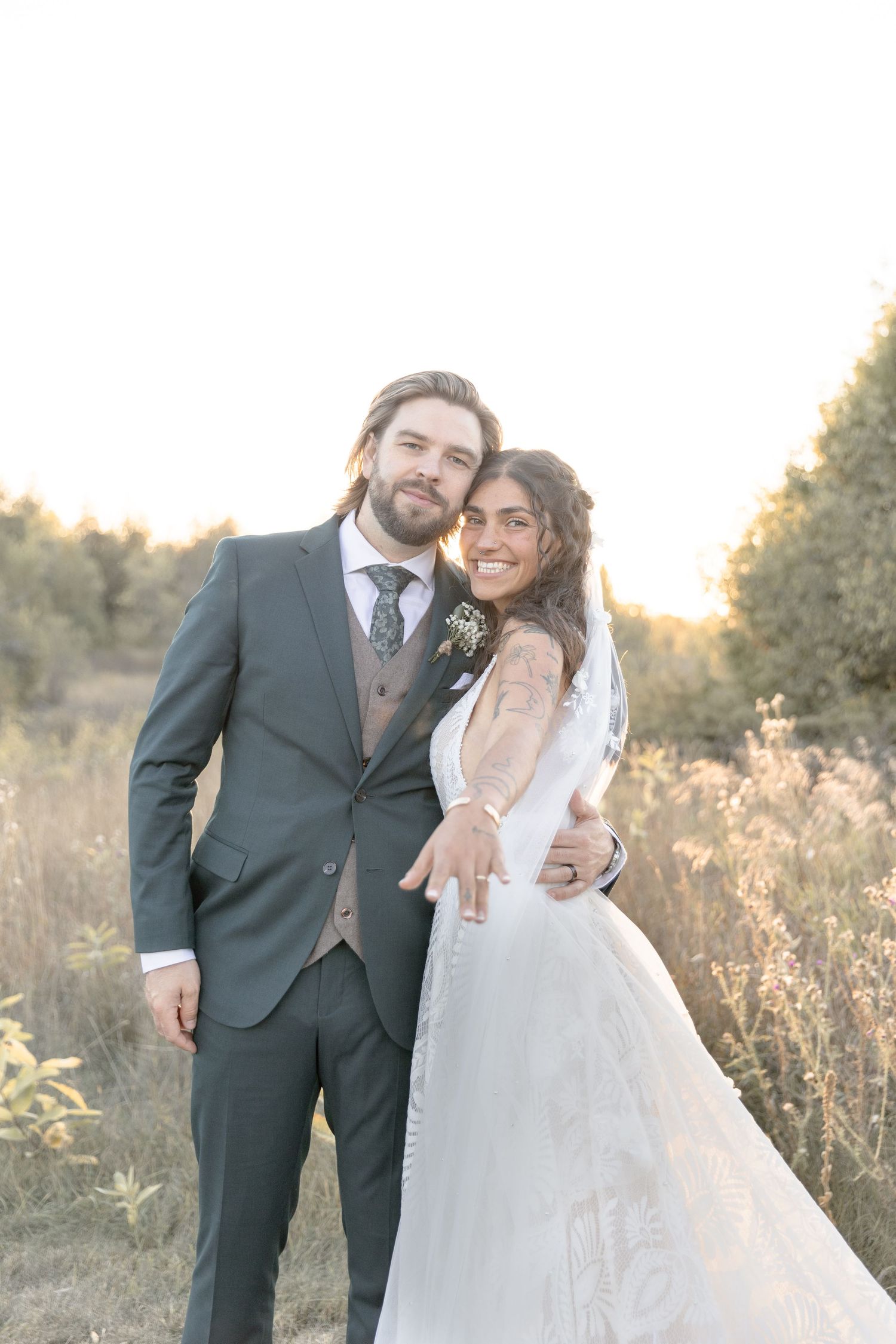 A romantic wedding couple poses in a sunlit field during golden hour wearing formal attire.
