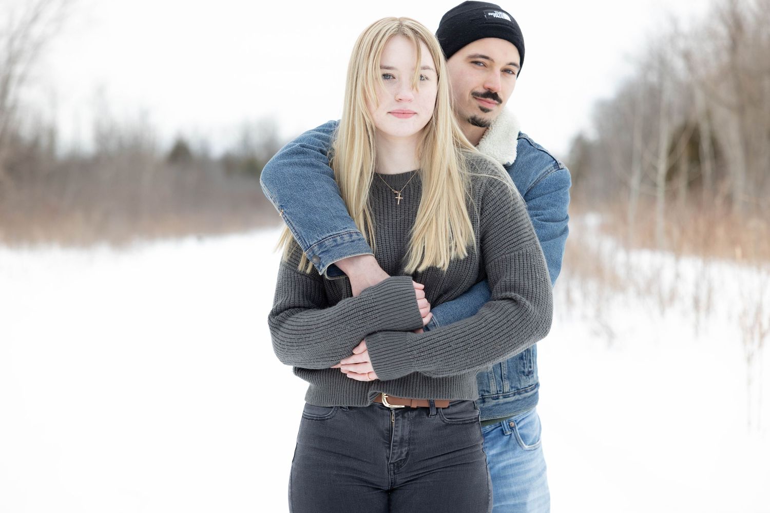 Casual winter portrait of a couple in denim and knitwear against a snowy landscape.