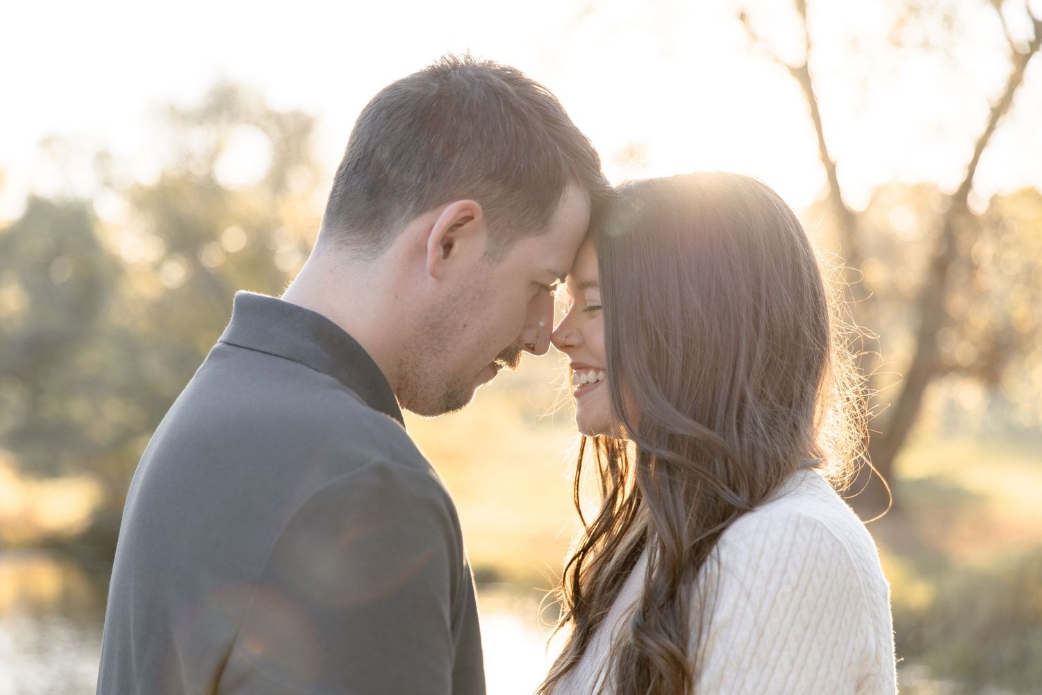 A couple shares a romantic moment during sunset in a golden field with soft backlit lighting.