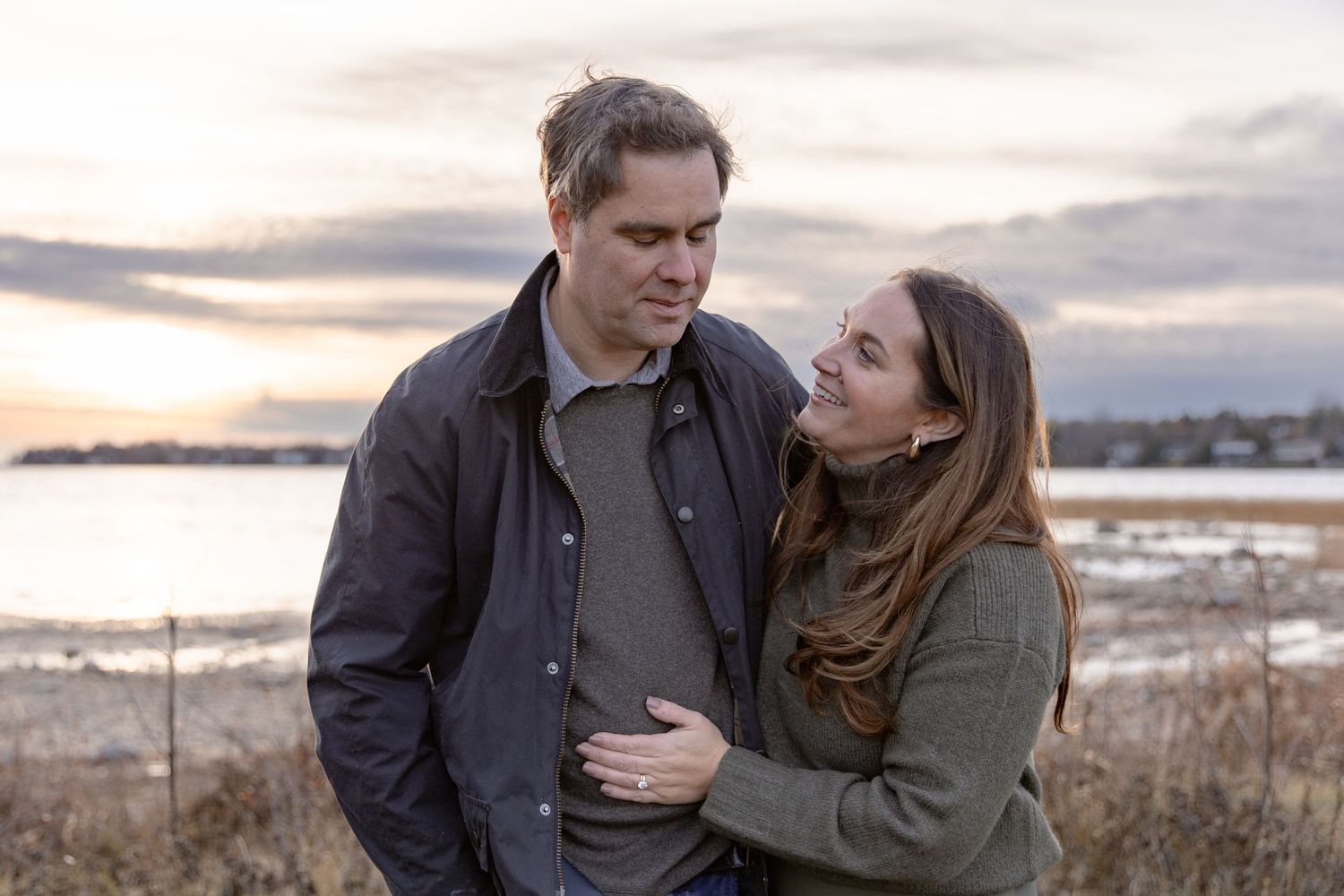 A couple shares an intimate moment together on a rocky beach during sunset.