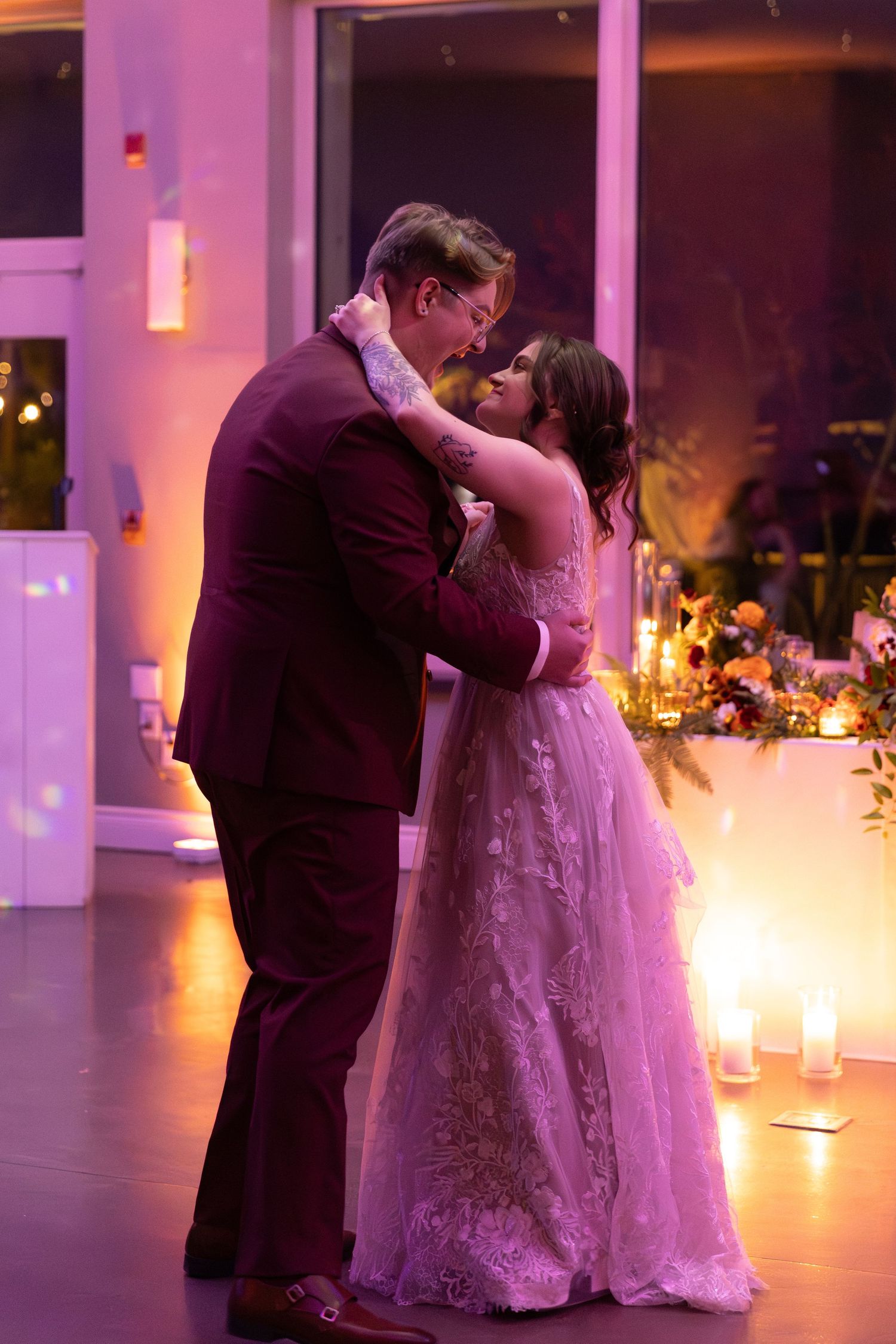 A romantic first dance between newlyweds in a reception venue with purple lighting and candlelit ambiance.