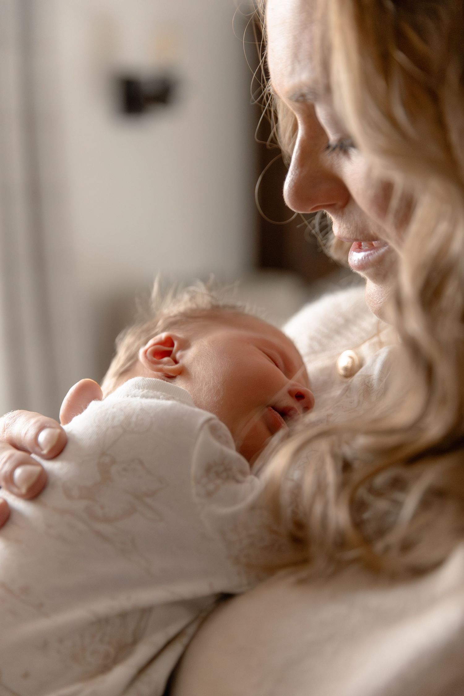 A tender moment between a sleeping newborn baby wrapped in white and a caregiver in soft natural lighting.