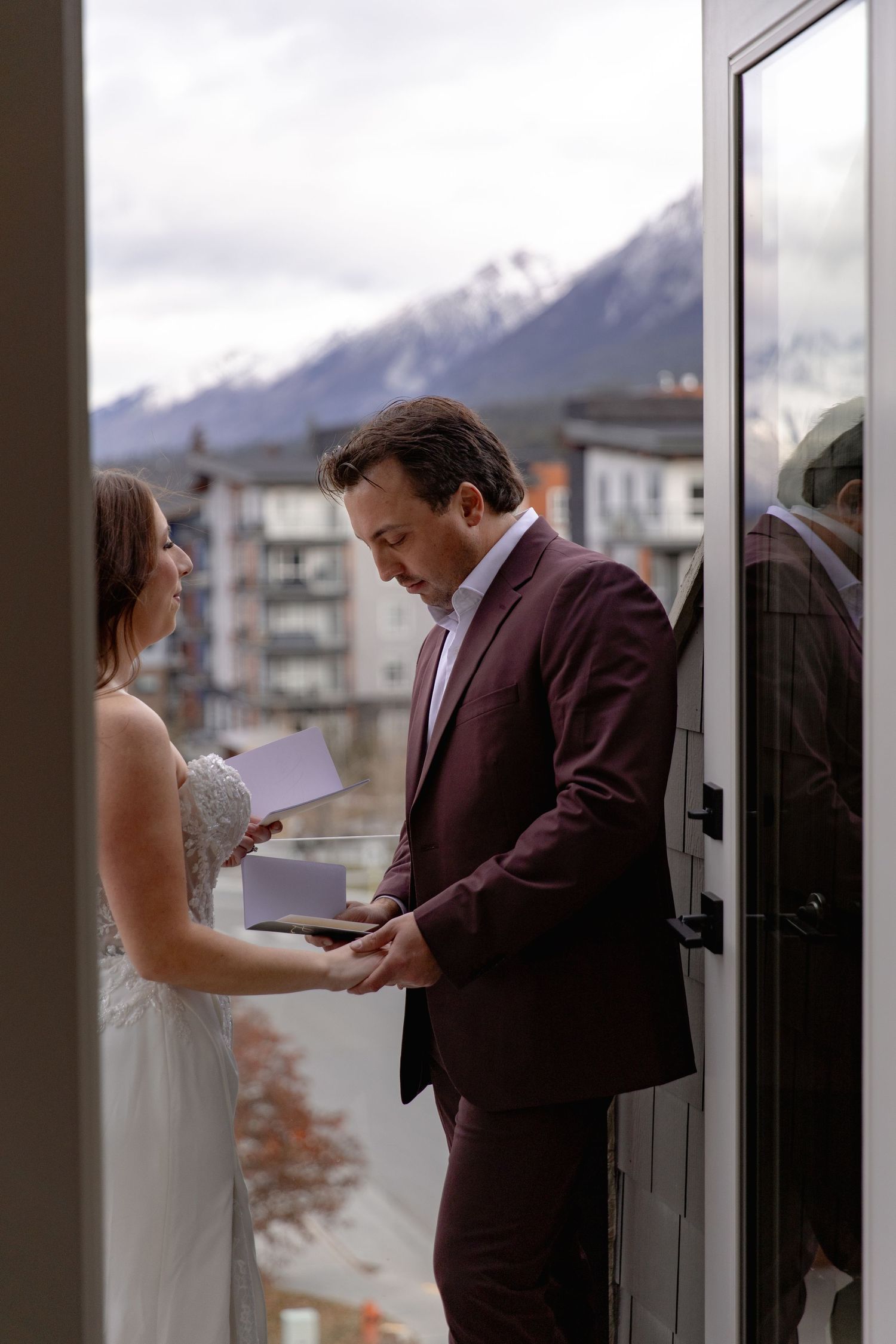 A couple exchanges vows during an intimate wedding ceremony on a balcony with snow-capped mountains in the background.