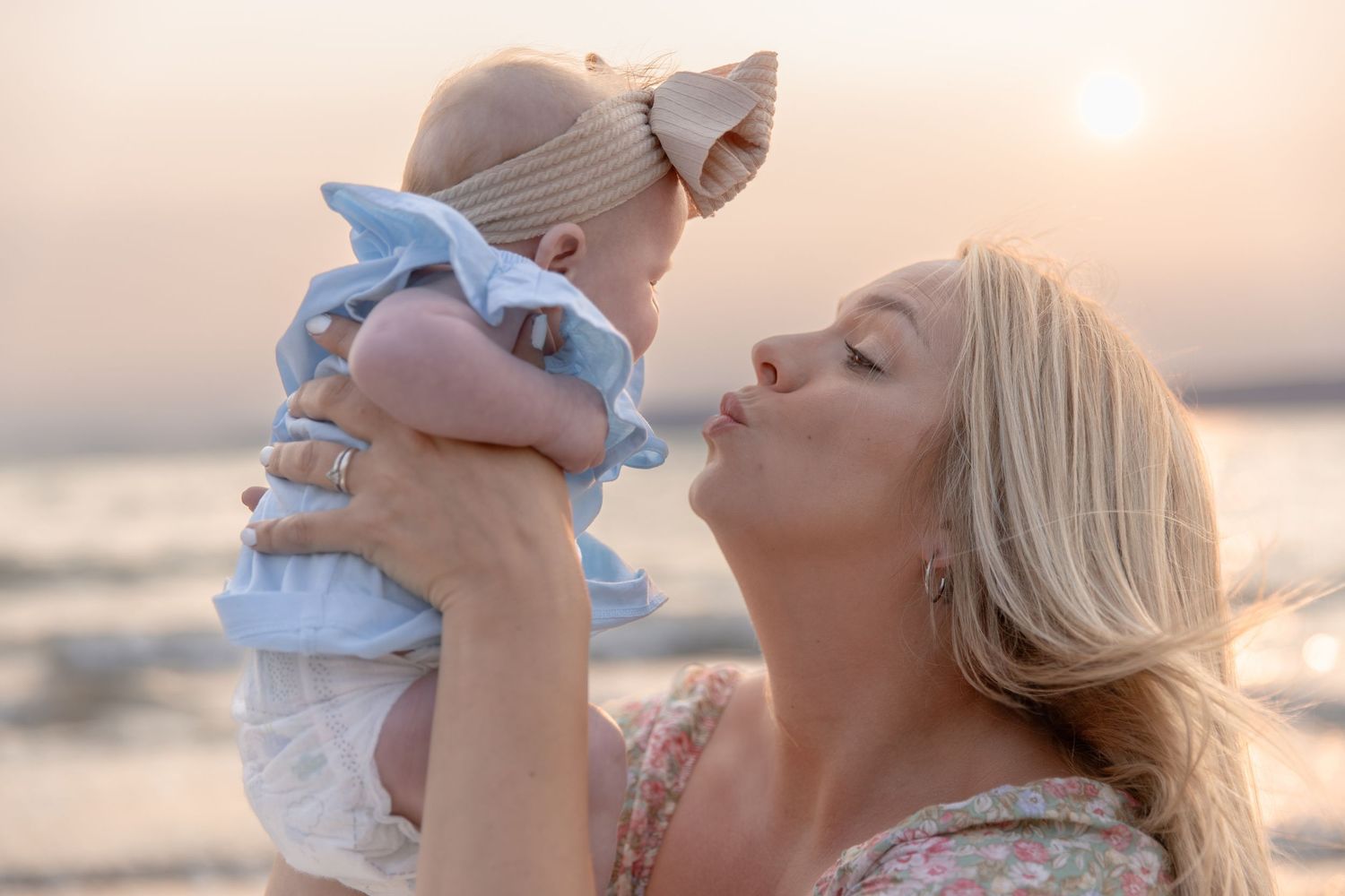 A tender moment between mother and baby at the beach during golden hour.