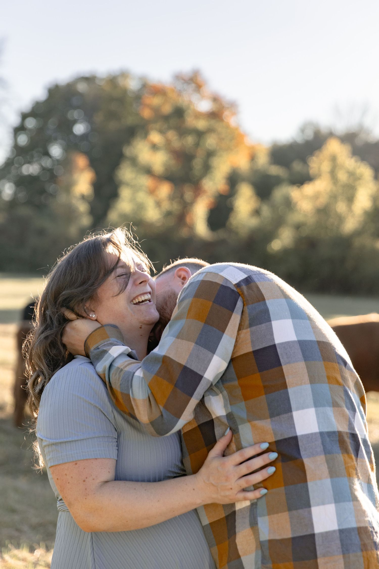 A couple shares a joyful embrace while laughing together in a sunlit autumn field.