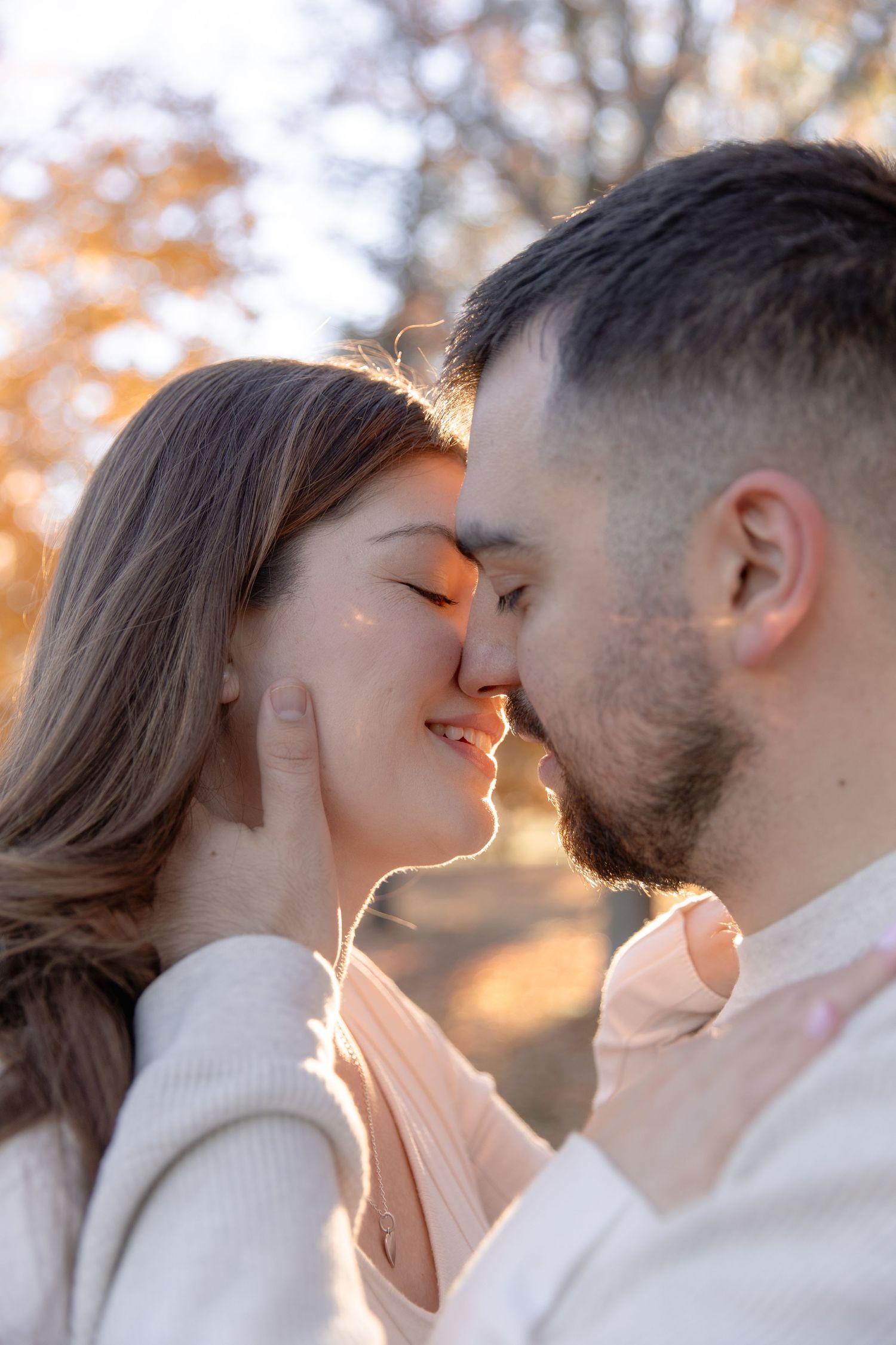 Intimate couple sharing tender moment in warm autumn sunlight with backlit glow.