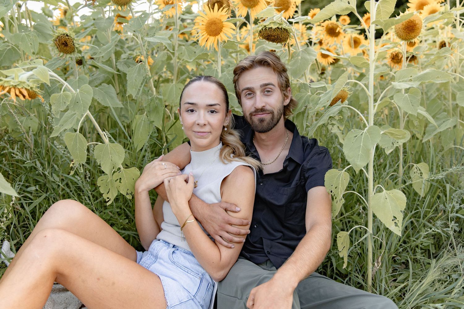 A couple poses together in a vibrant sunflower field during a summer photoshoot.