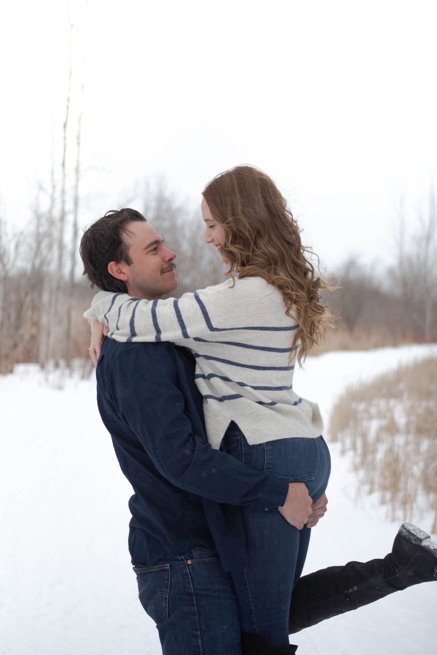 A joyful couple embraces in the snow during their winter engagement photoshoot.