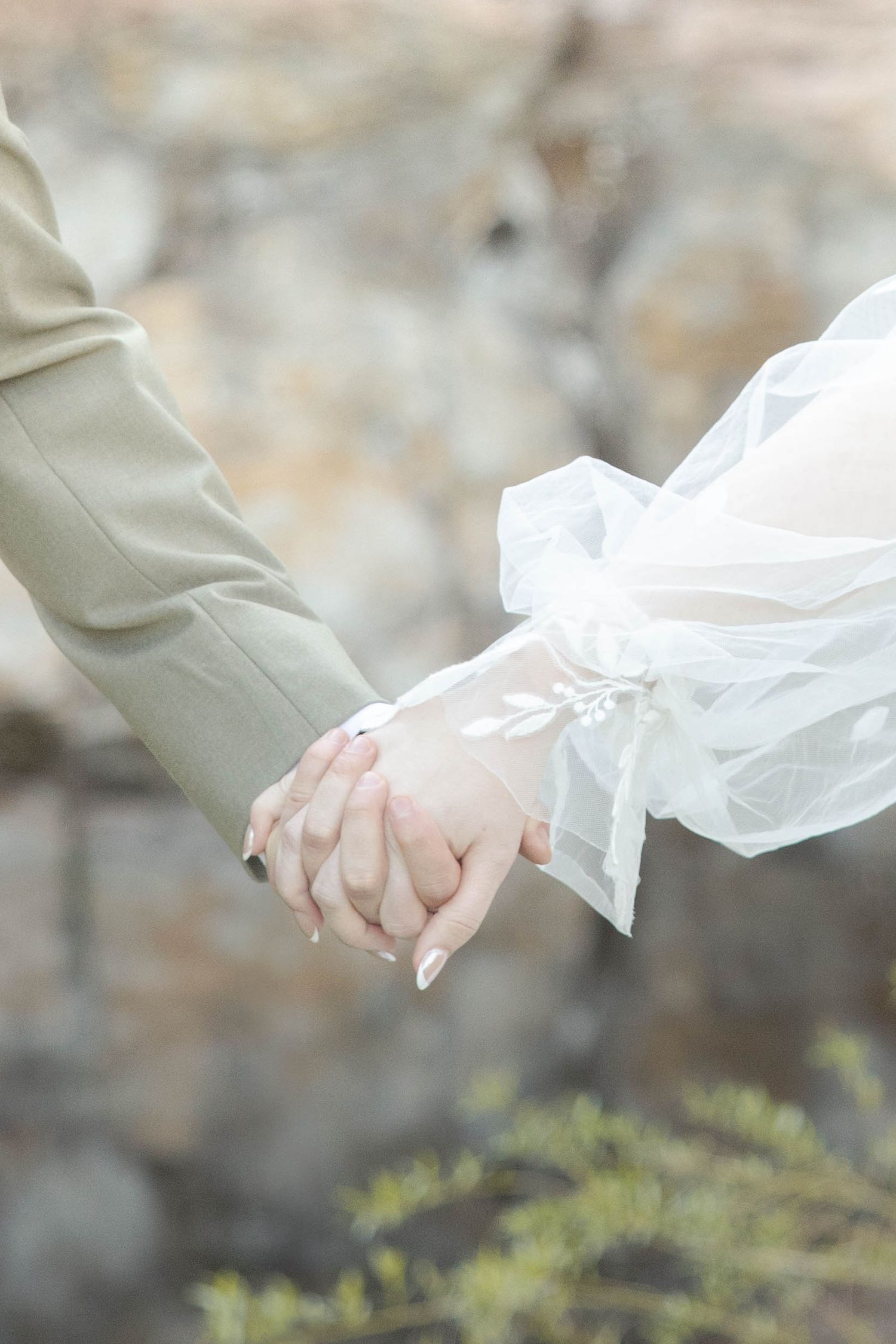 A romantic close-up of two people holding hands, with a flowing white tulle wedding veil visible in soft focus.