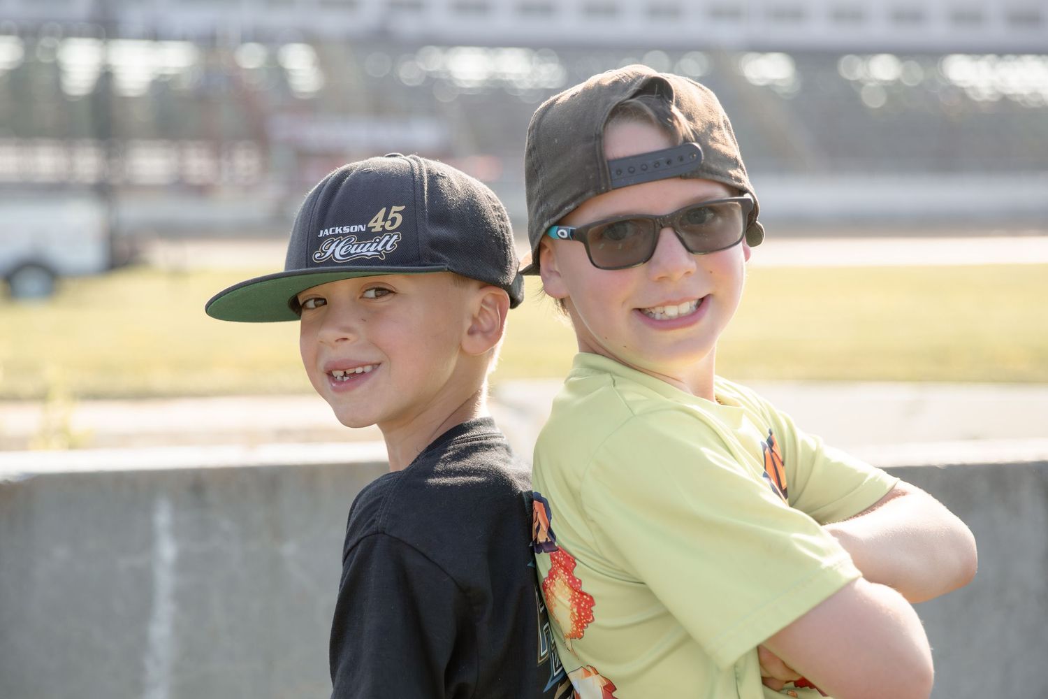 Two visitors watch an event through binoculars at a sunny outdoor venue.