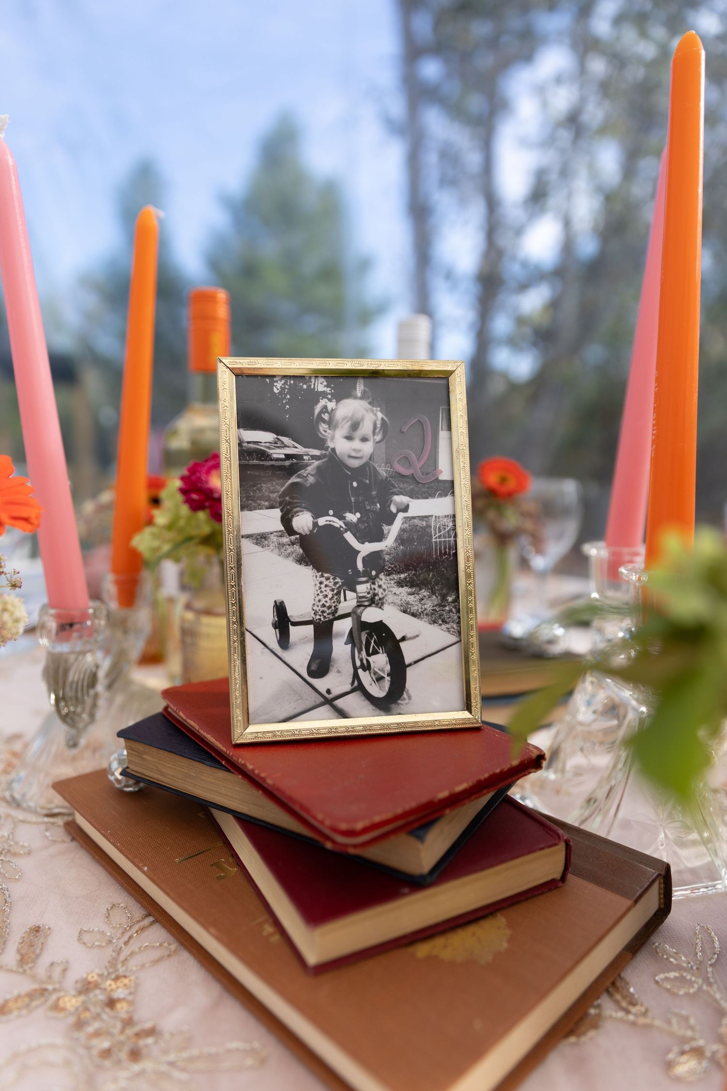 Vintage black and white photographs displayed on stacked books with orange and pink candles creating an elegant table setting.