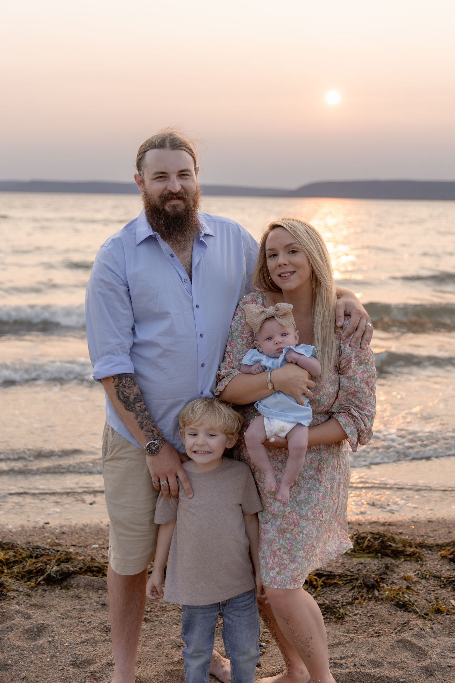 A family stands together on a beach at sunset with a serene ocean backdrop.