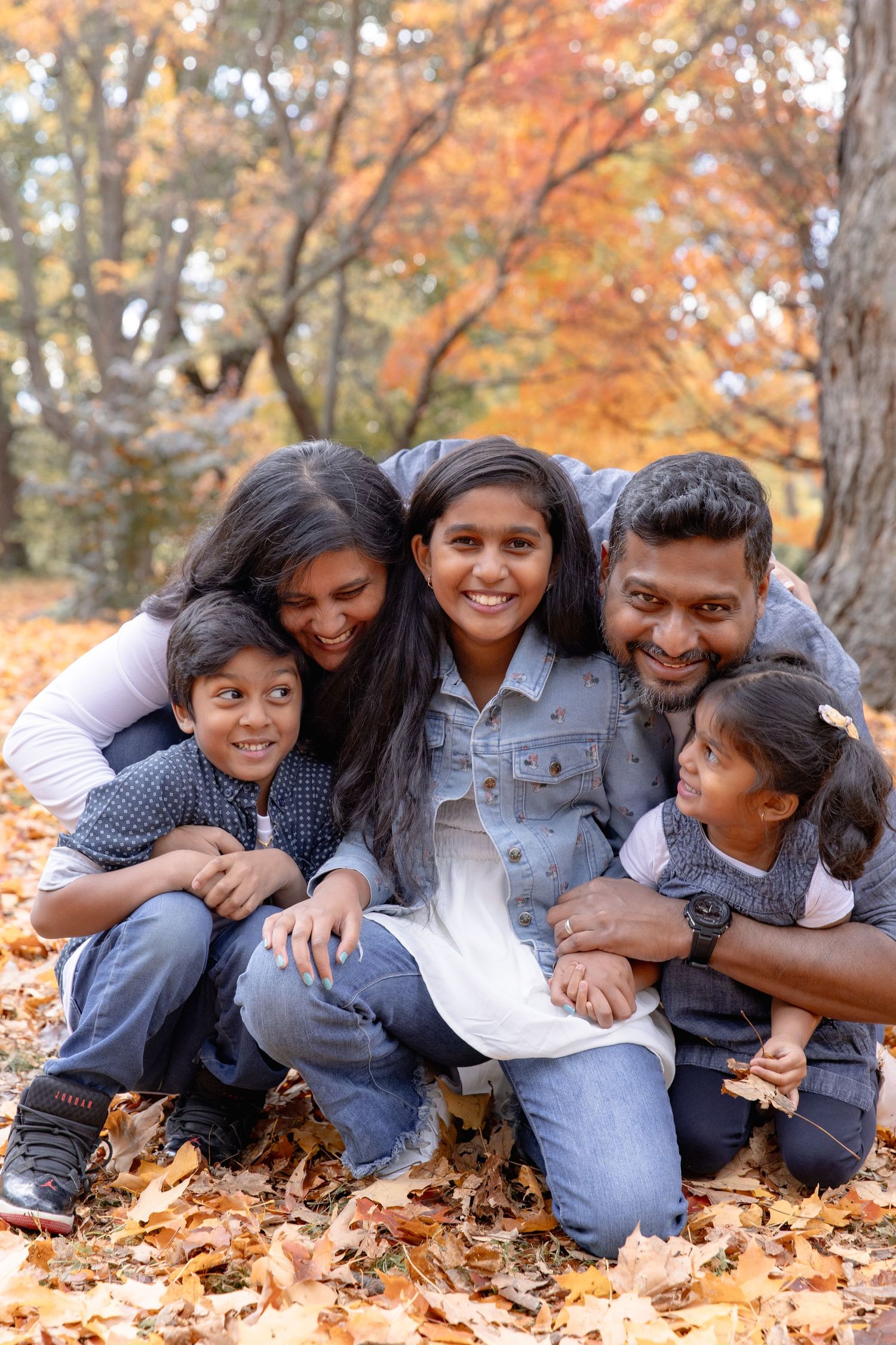 A family group poses together while lying in colorful autumn leaves during a fall photo session.