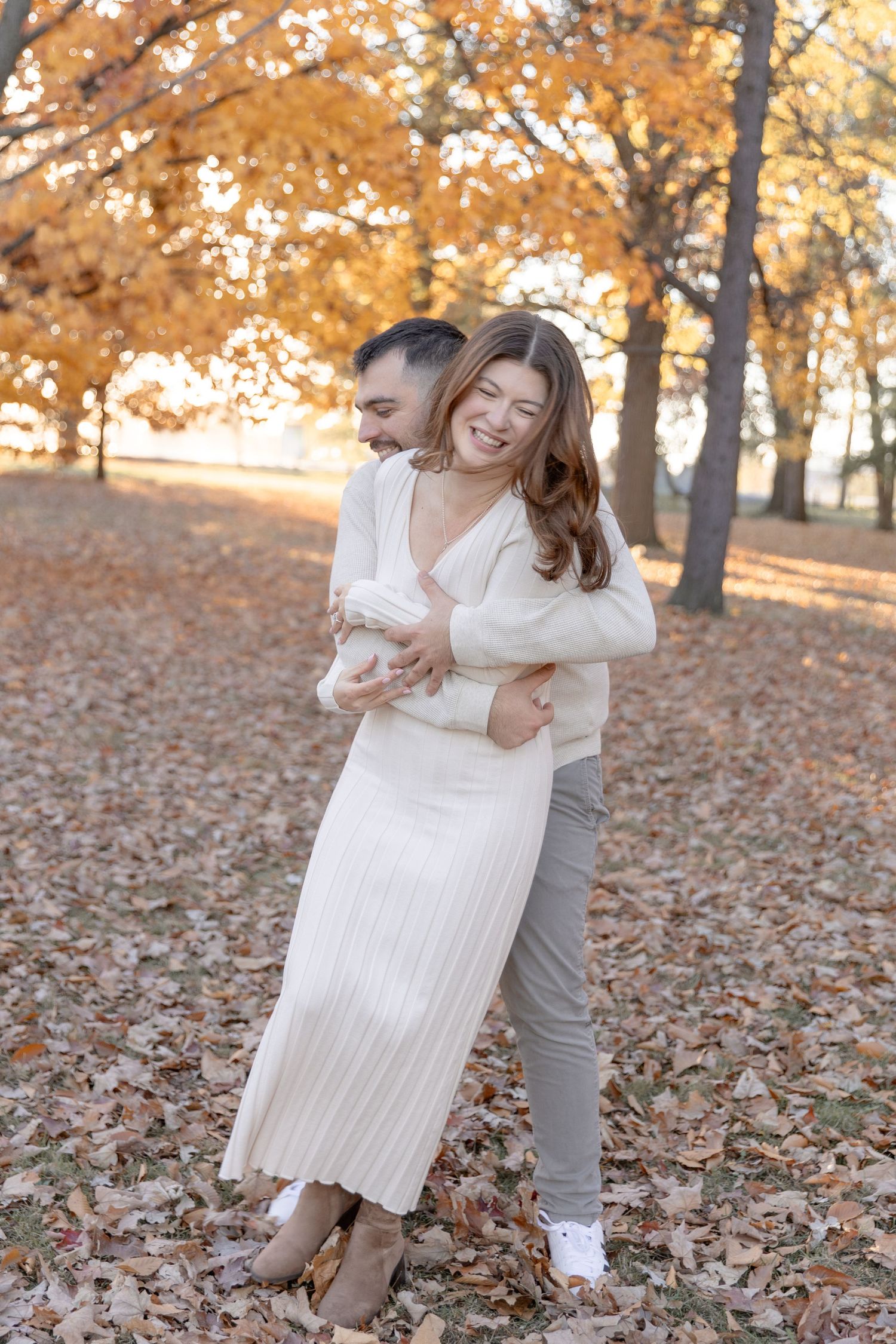 Couple embracing and laughing among fall foliage with golden autumn trees in background.