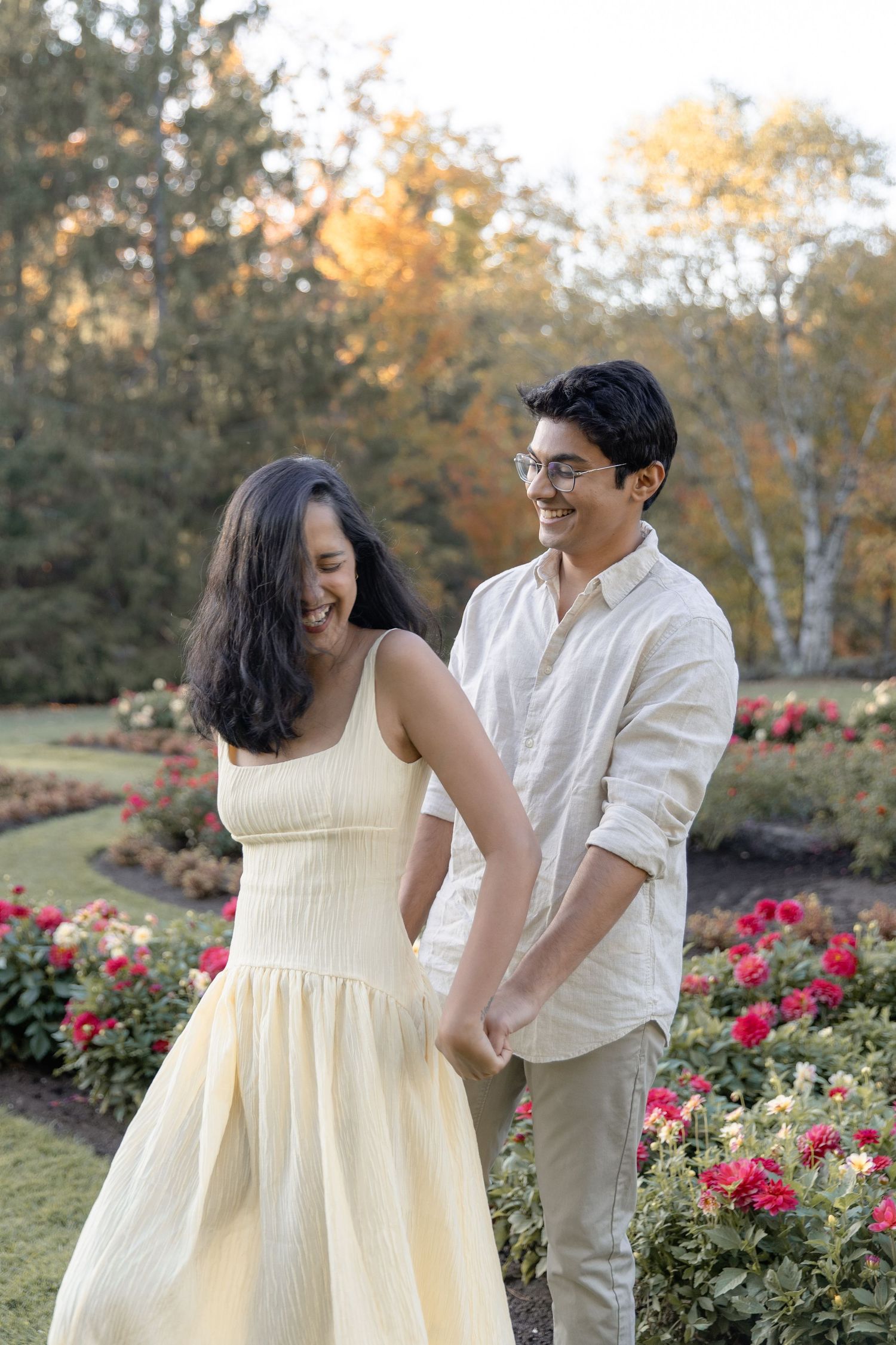 A couple laughs and embraces in a rose garden during an outdoor photo session.