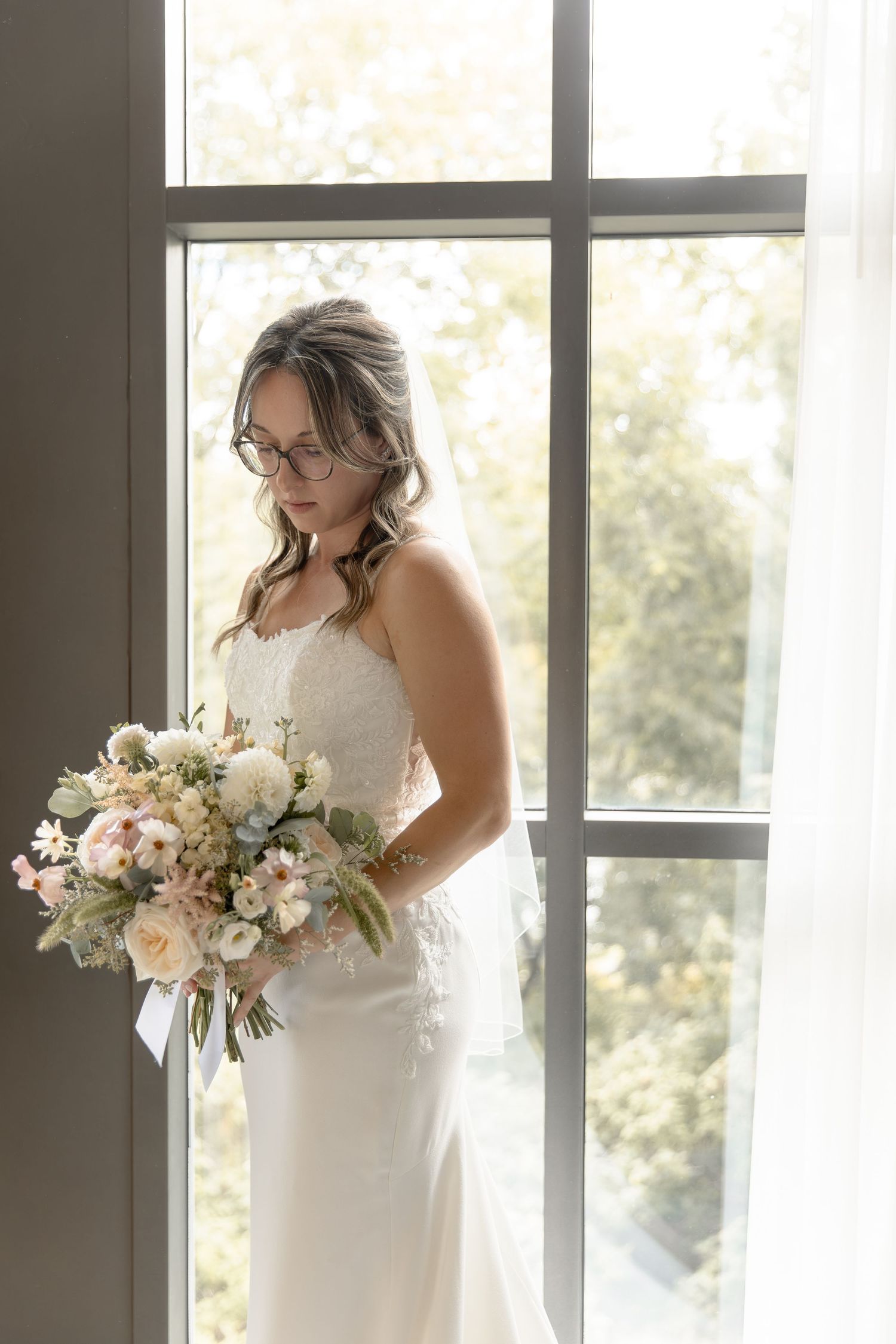 Elegant bridal portrait showing a white wedding dress and beautiful pastel bouquet by sunlit windows.
