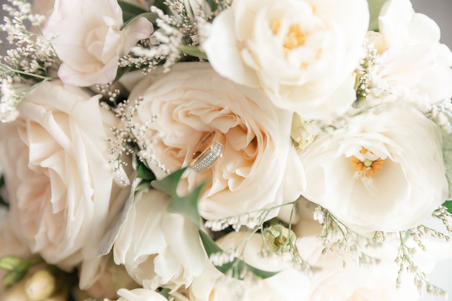 Close-up of wedding rings nestled among white and blush garden roses in an elegant bridal bouquet.