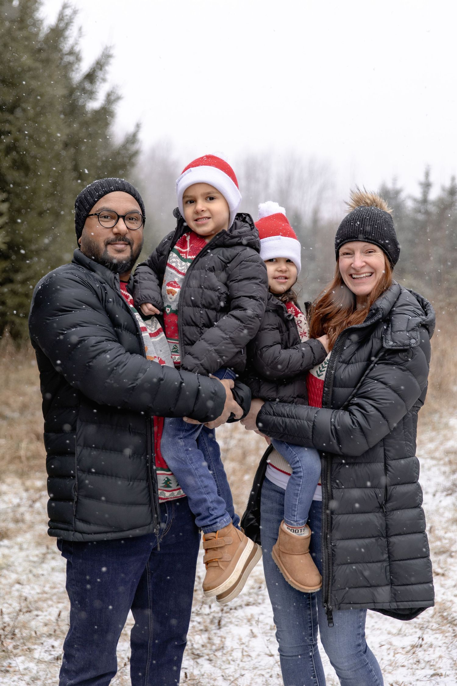 A family wearing winter coats and holiday accessories poses together in the snow during winter.