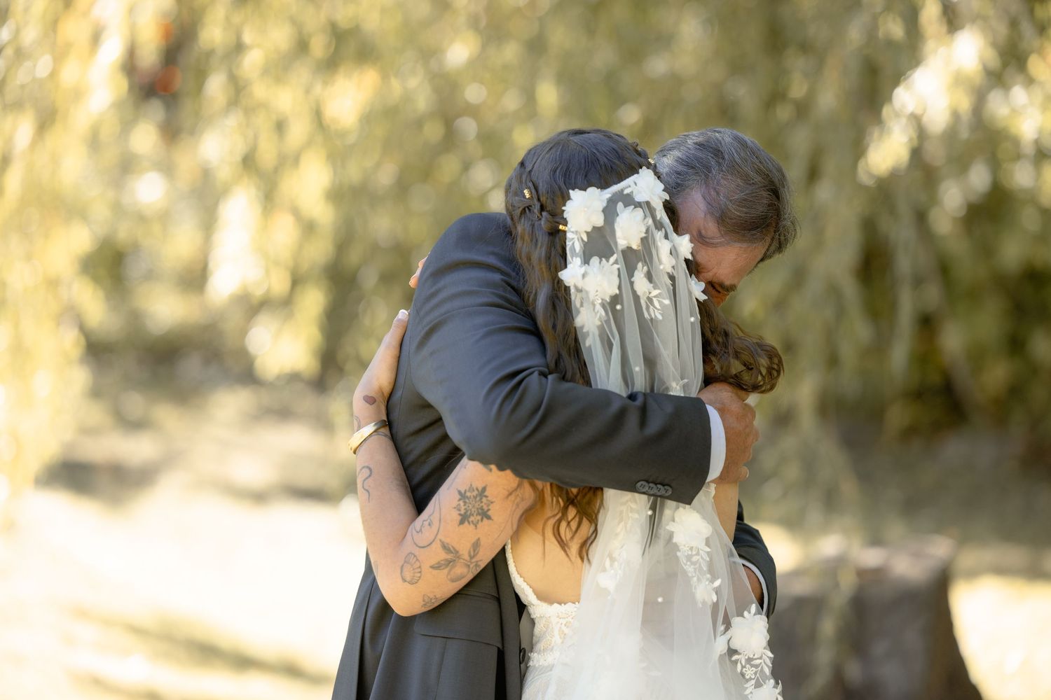 A couple shares a romantic moment while embracing against a tree in a sunlit outdoor setting.