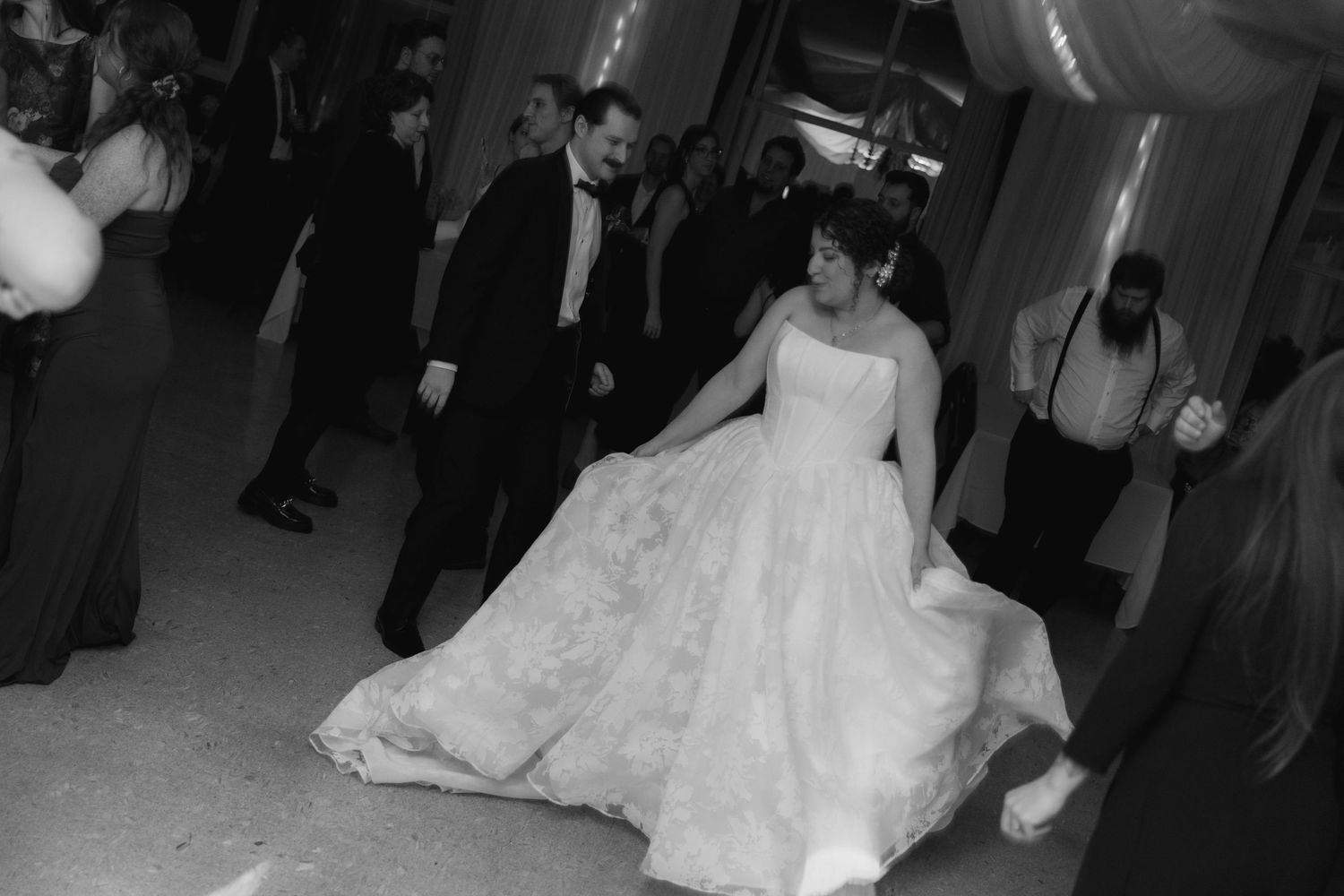 A bride in a flowing white ball gown dances at a wedding reception in black and white photography.