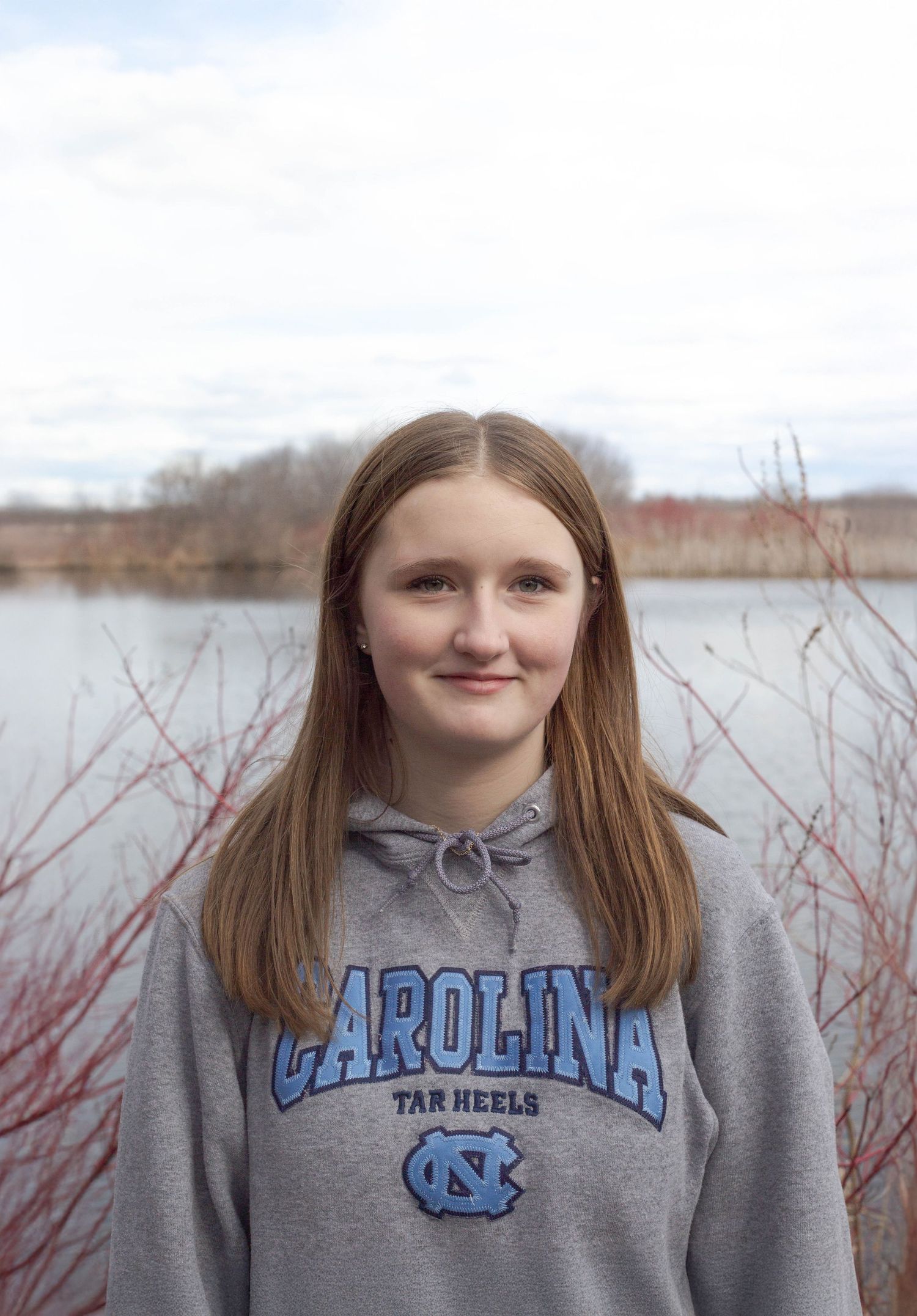 Student wearing a Carolina sweatshirt stands near a lake on an overcast day.