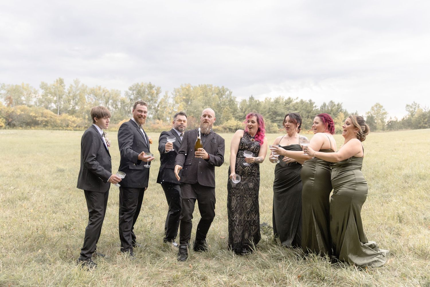 Wedding party standing in a line outdoors with their backs turned to the camera in a grassy field.