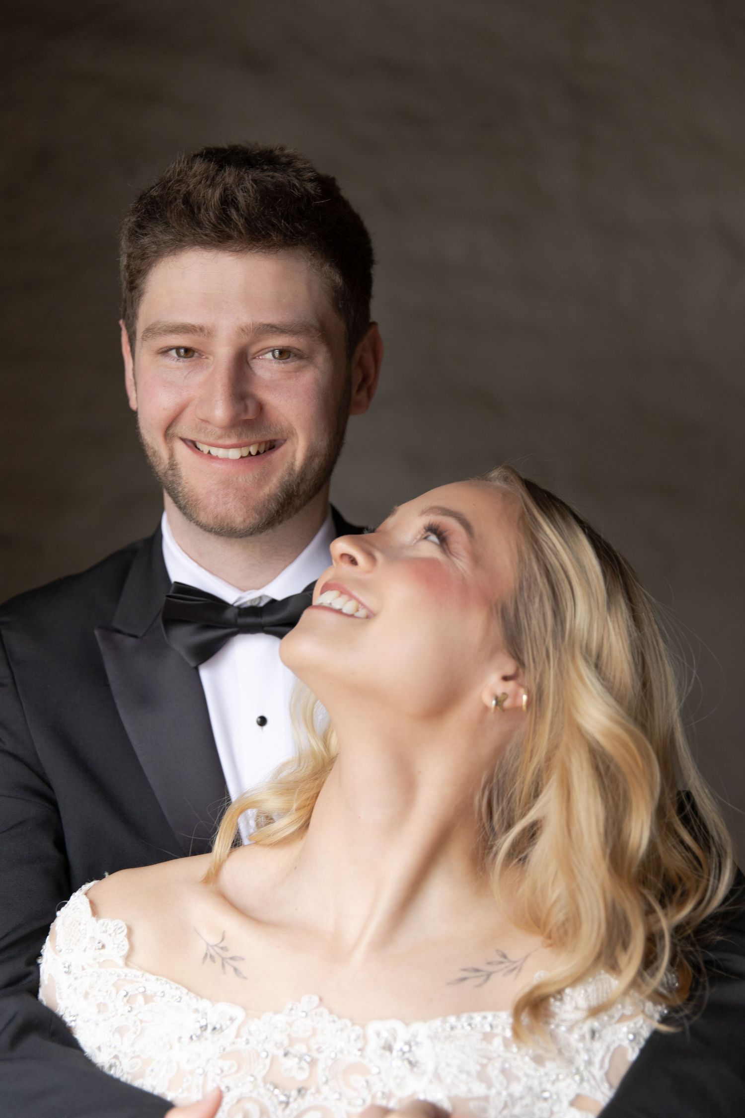 Wedding couple in formal attire sharing a romantic moment against a dark background.