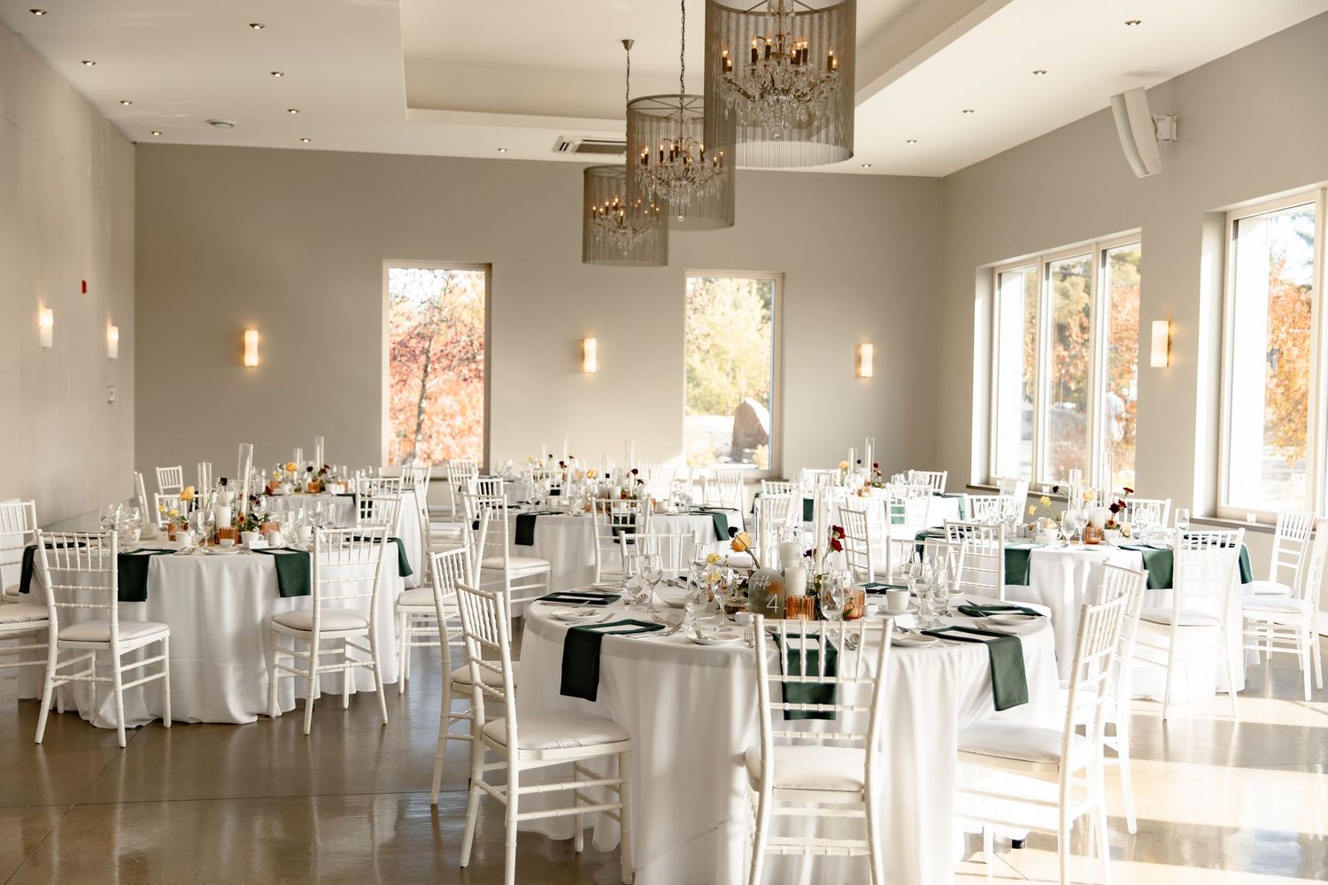 Modern white event space with elegant table settings and hanging pendant lights in a bright, airy room.