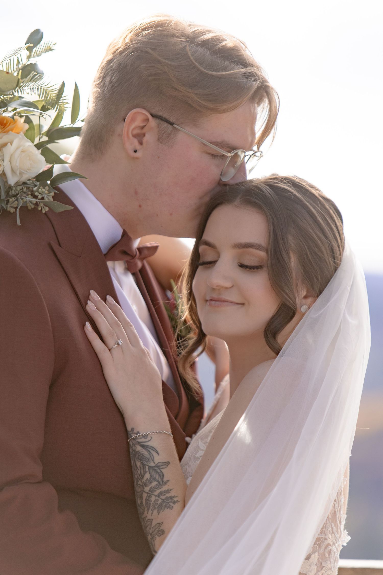 Intimate wedding portrait of a couple embracing in warm sunlight with flowing veil and rustic brown suit.
