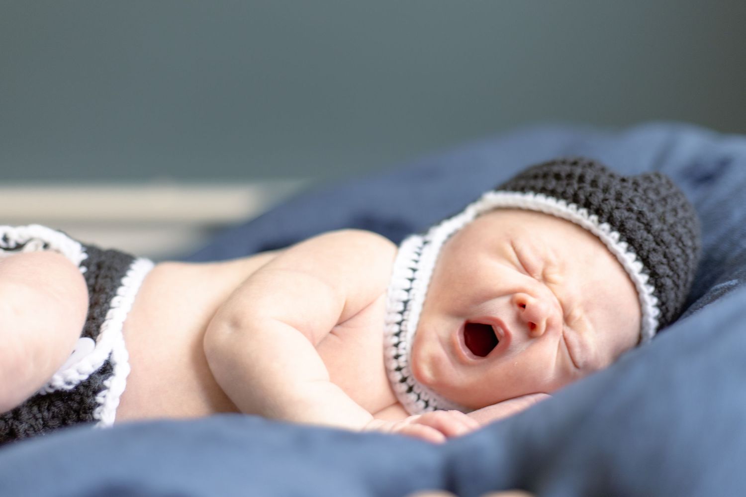 A sleeping newborn baby wrapped in soft gray blankets lies peacefully against a textured background.