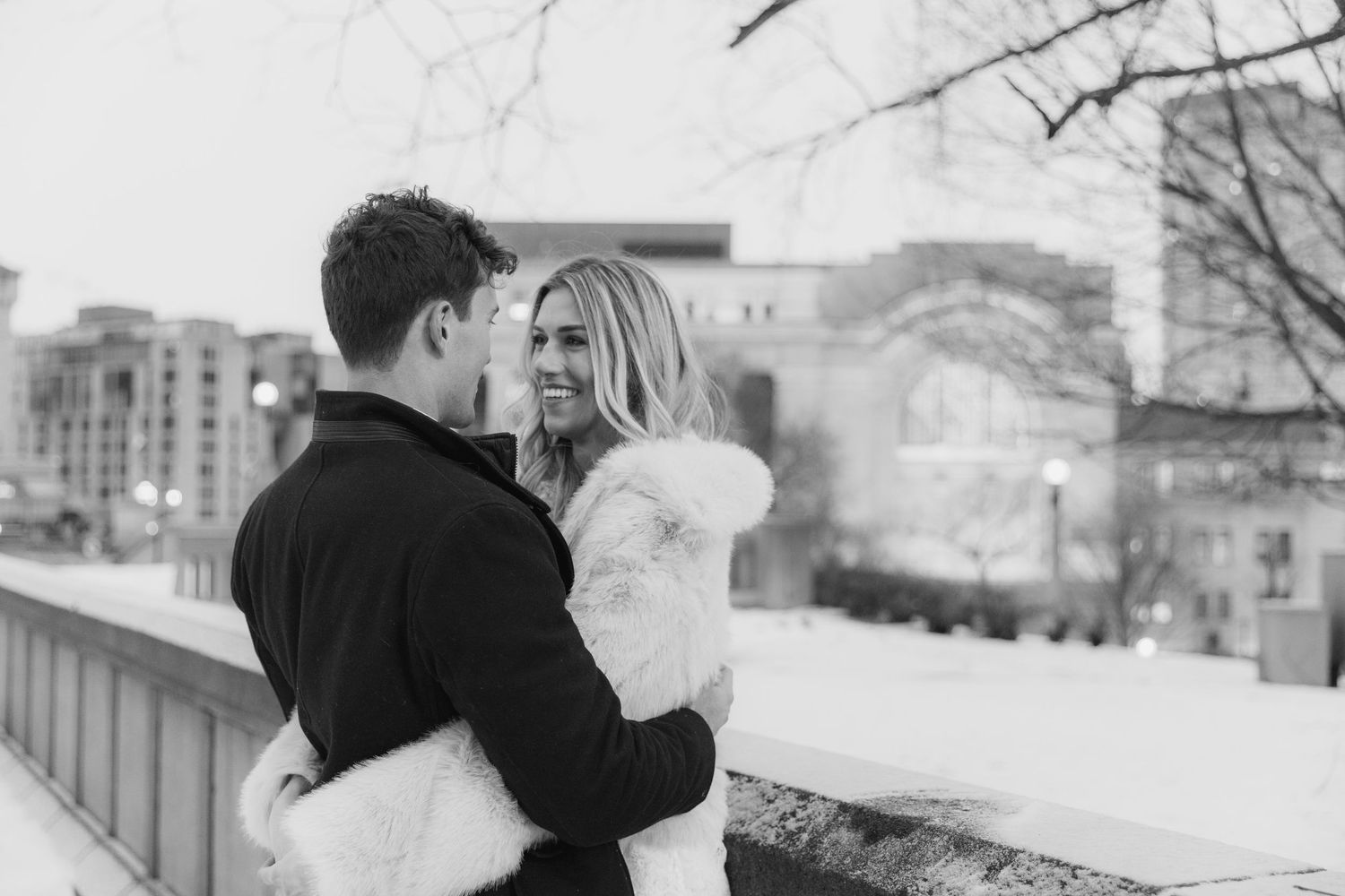 A romantic couple sharing an intimate kiss outdoors in winter with snow-covered scenery in the background.