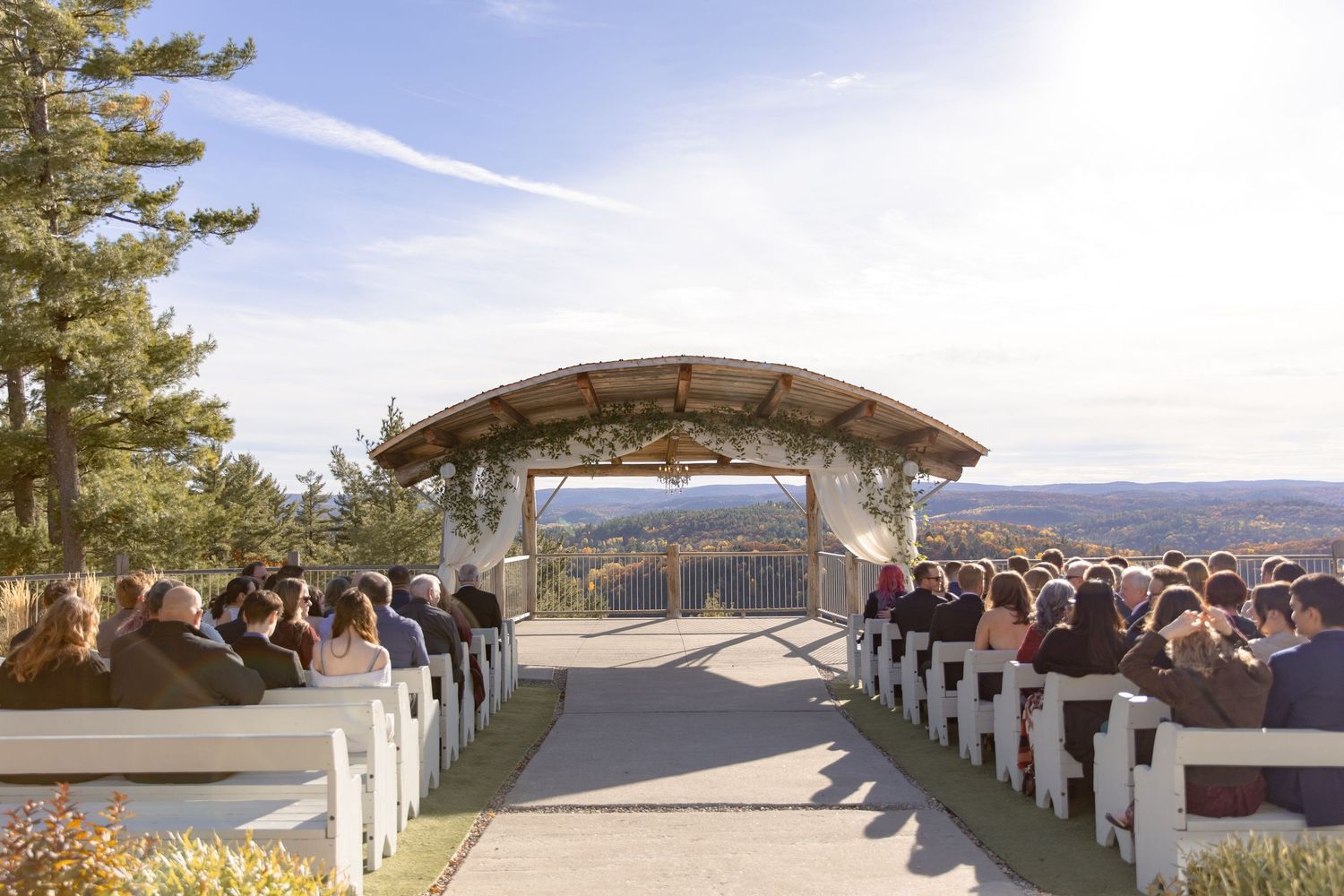 A panoramic view of a wedding ceremony setup with white chairs on a mountain overlook with scenic valley views.