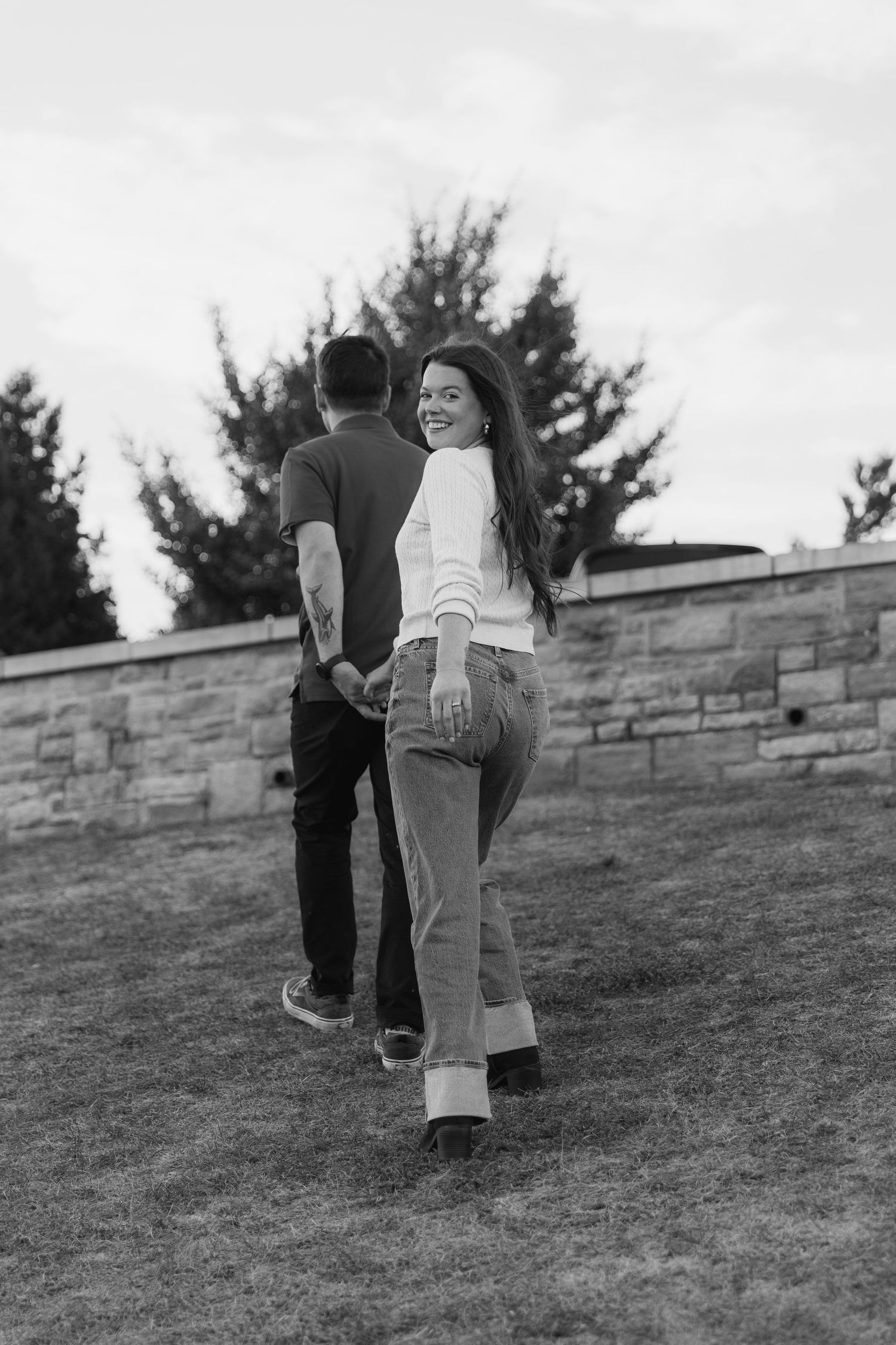 A couple walks together on a grassy hillside in a black and white photograph series.