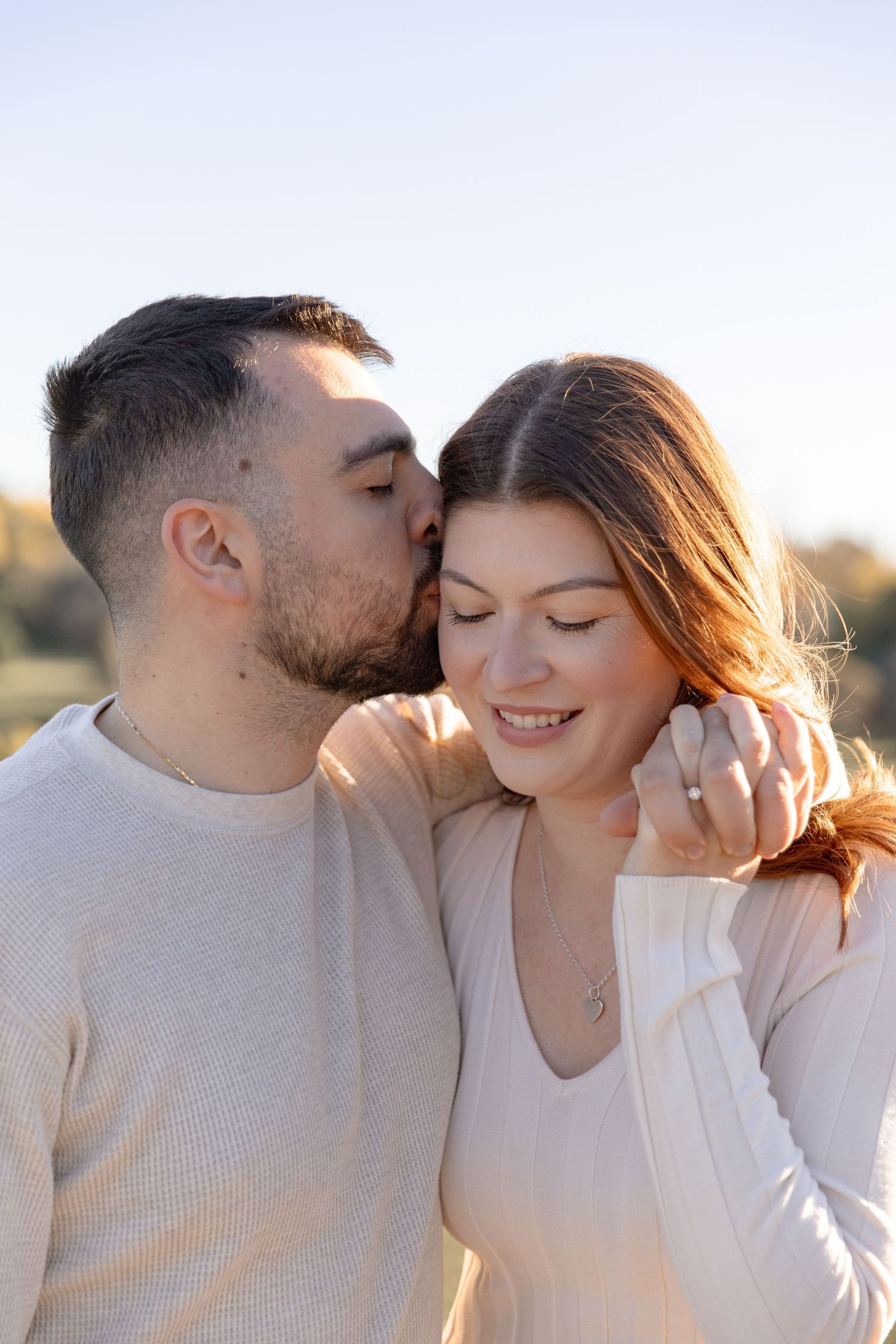 A romantic couple in white sweaters sharing tender moments during a golden hour photoshoot.
