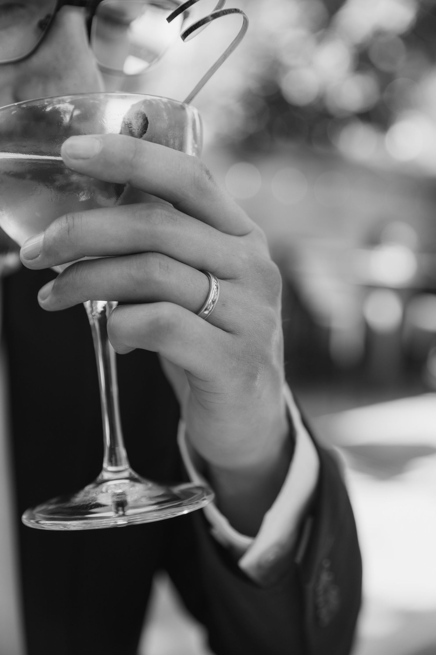 A close-up view of hands holding delicate wine glasses in black and white photography.