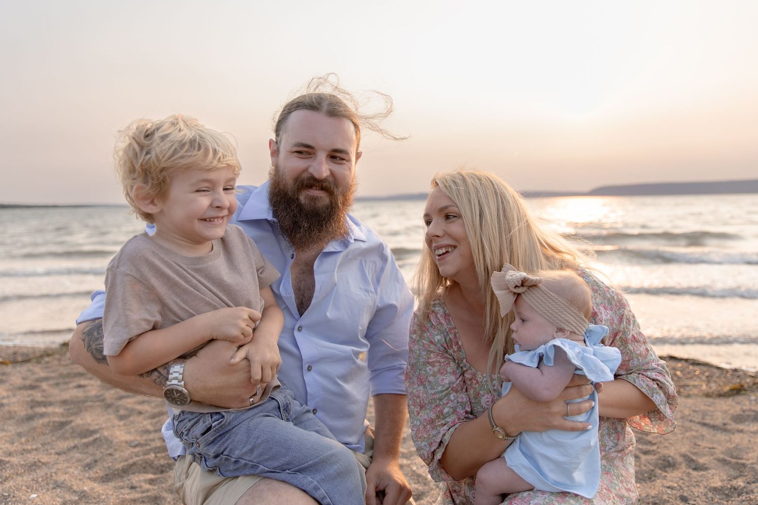 A happy family sitting together on a sandy beach at sunset with waves in the background.
