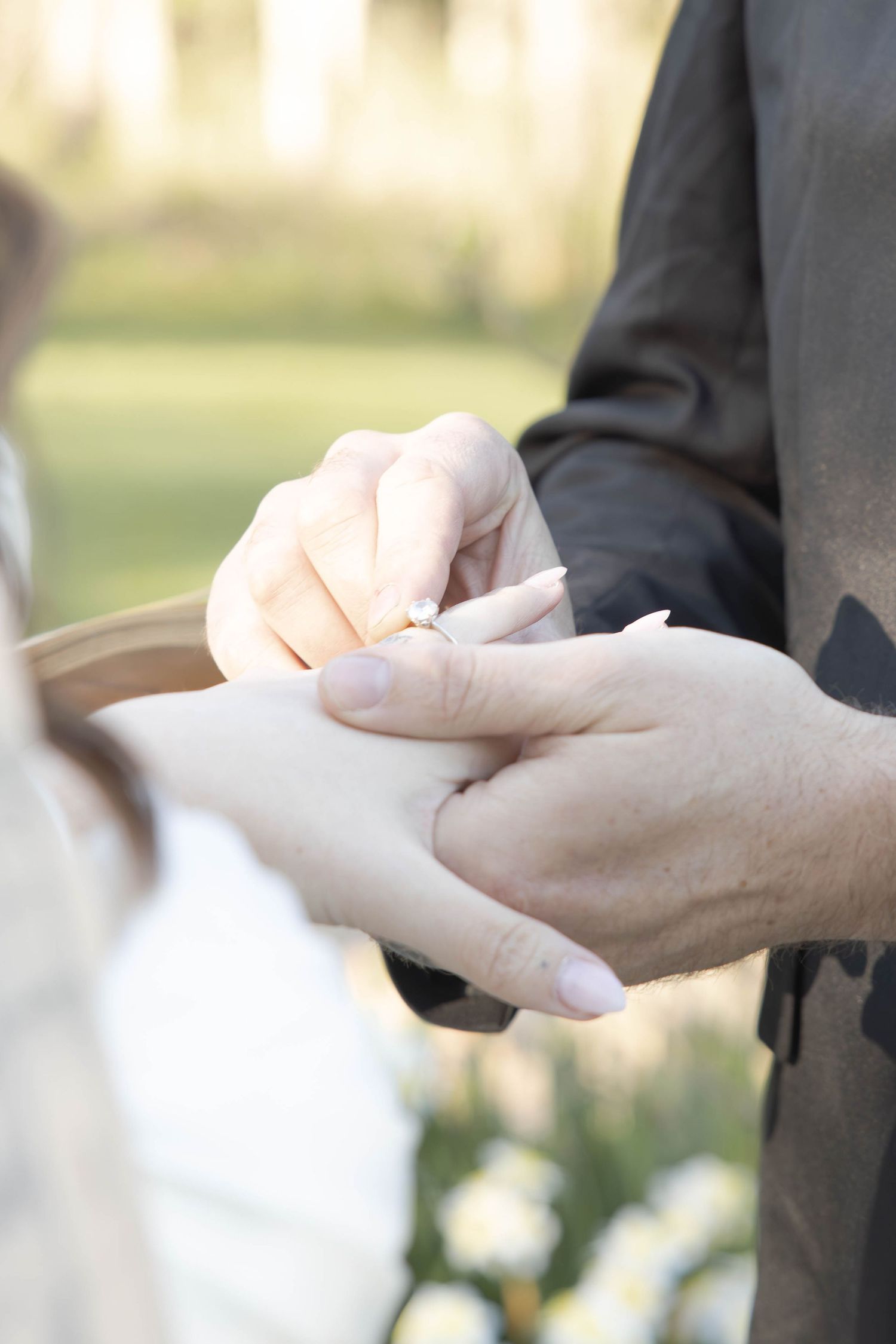 Close-up of hands exchanging wedding rings during an outdoor ceremony.