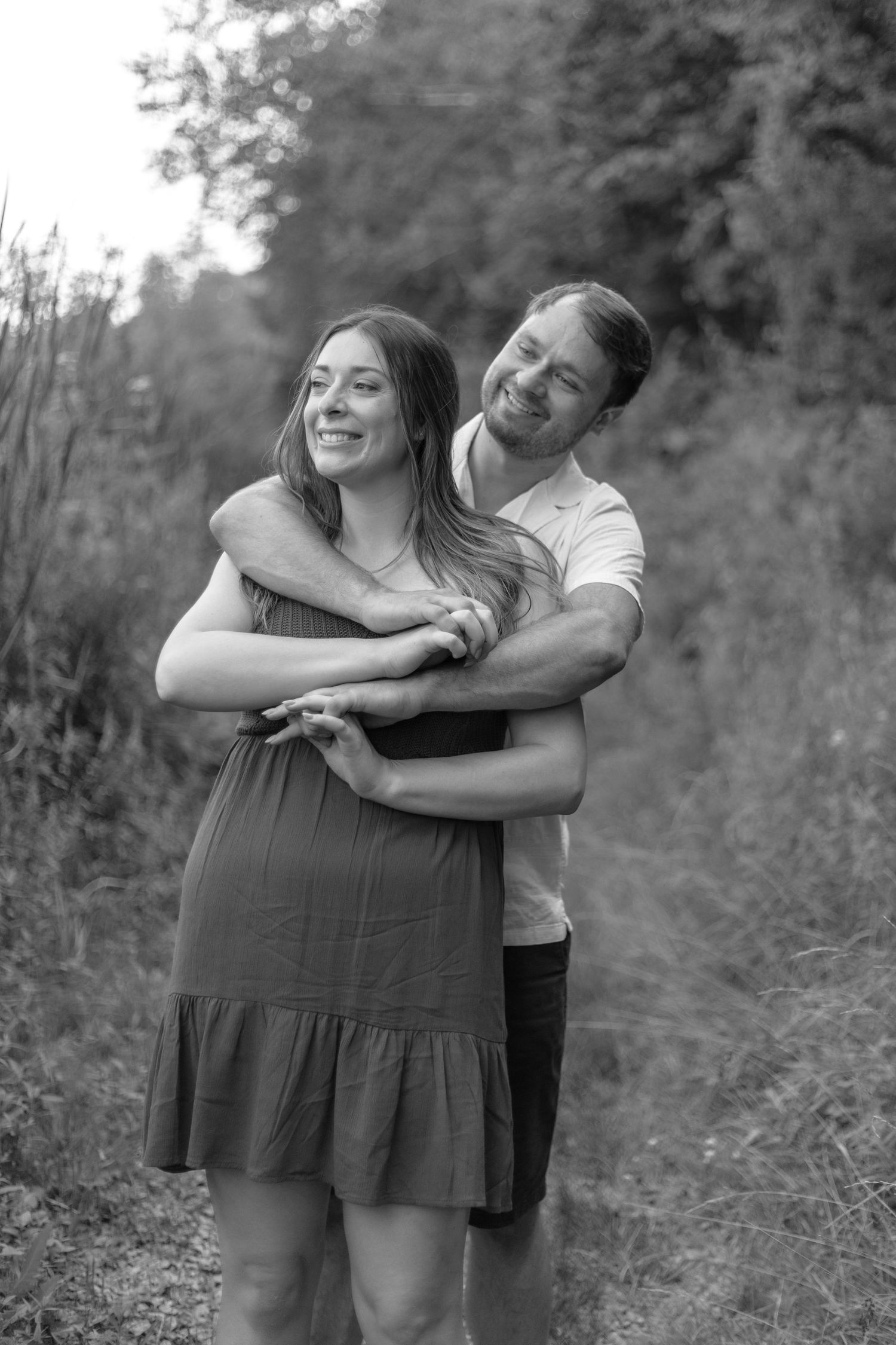 A loving couple embraces outdoors in a black and white photo series showing playful and candid moments in nature.