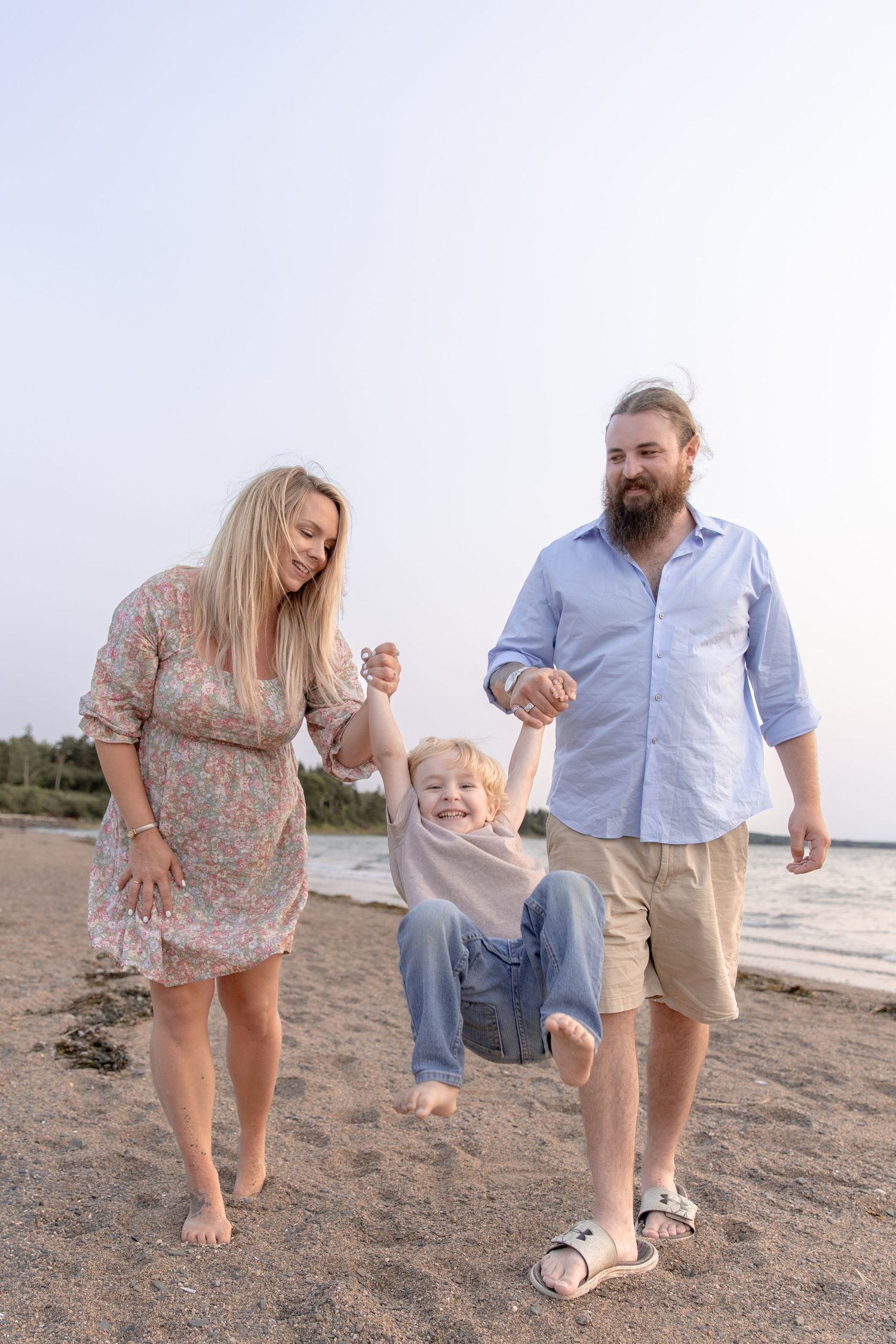 A family walks together on a sandy beach, holding hands and enjoying a playful moment at the seashore.