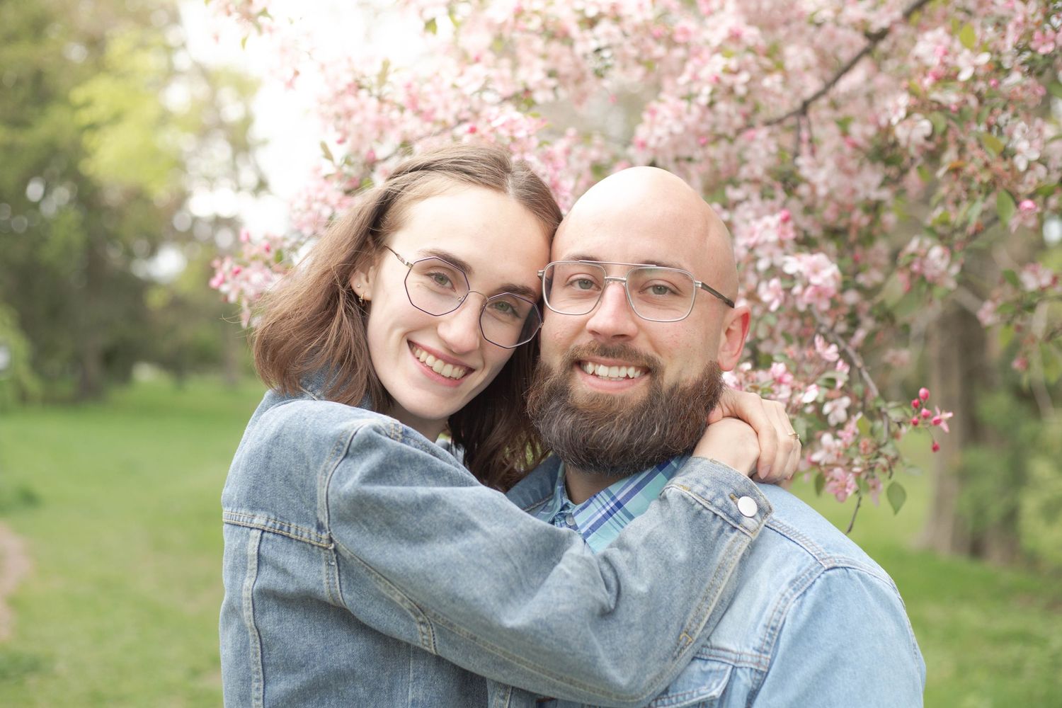 A couple embraces under blooming cherry blossom trees in a spring garden setting.