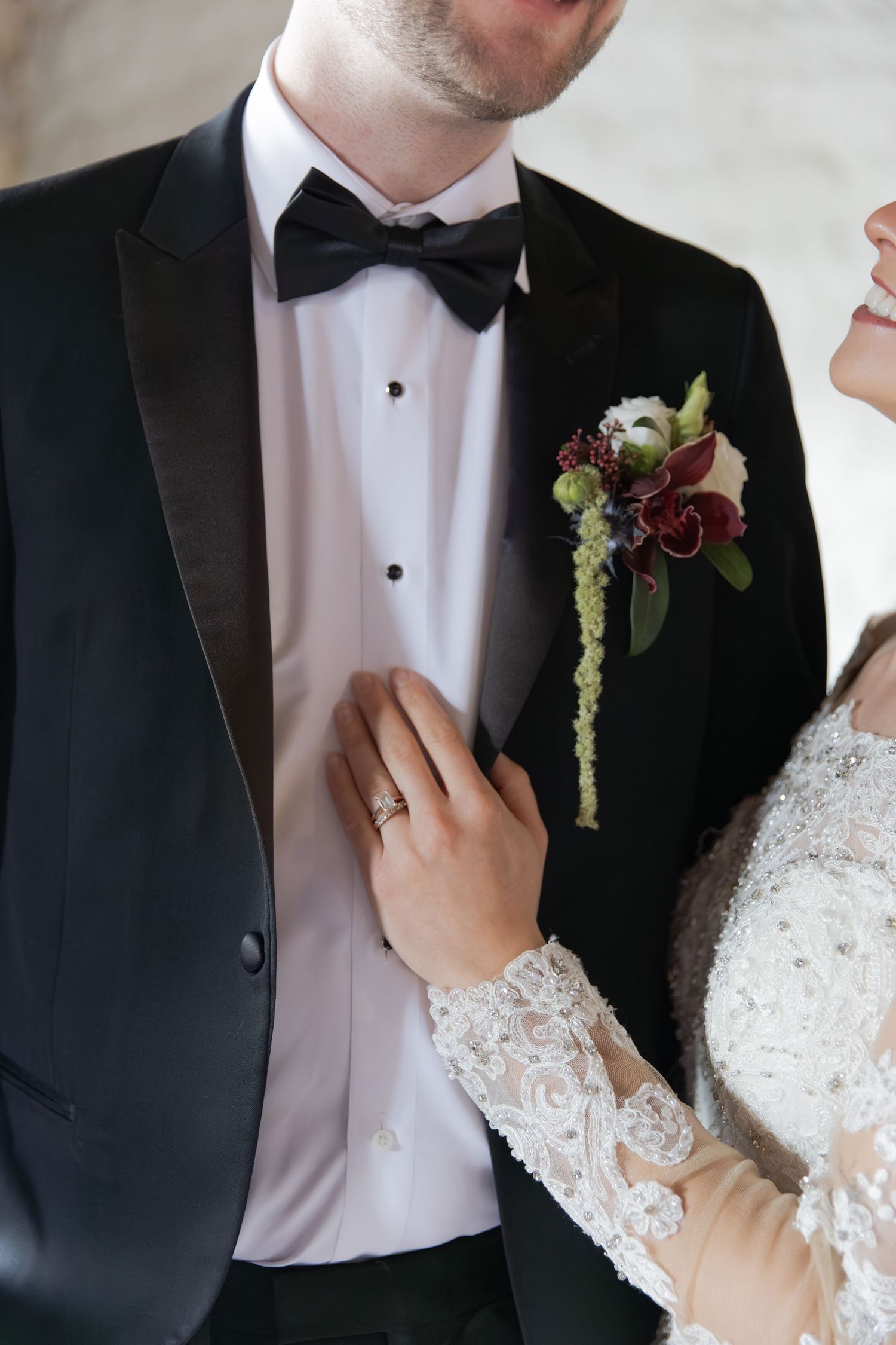 Close-up details of formal wedding attire showing black tuxedo lapel and white lace dress sleeve.