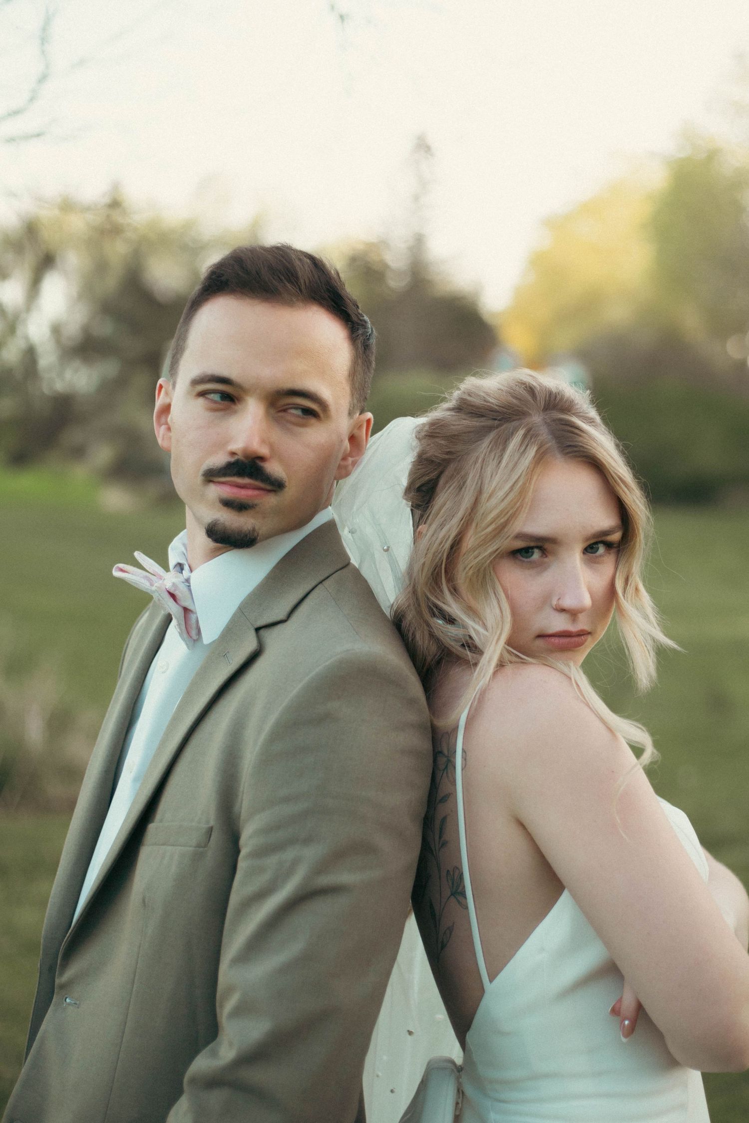 A couple in formal wear poses playfully in a park setting with mint green and olive colored attire.