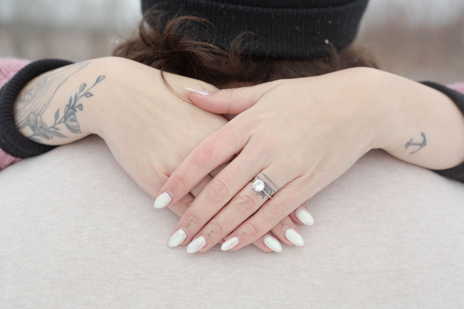 Close-up of hands showing engagement ring with delicate tattoo details.
