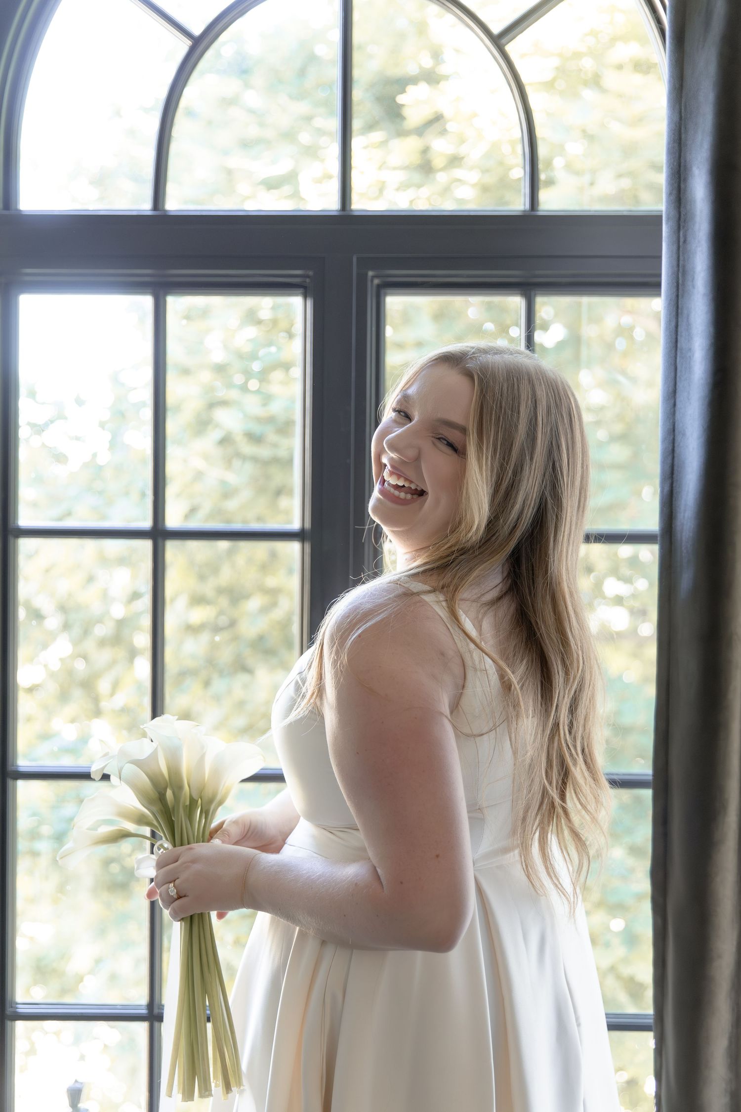 Joyful moment in front of arched windows with sunlight streaming in while wearing a white dress.