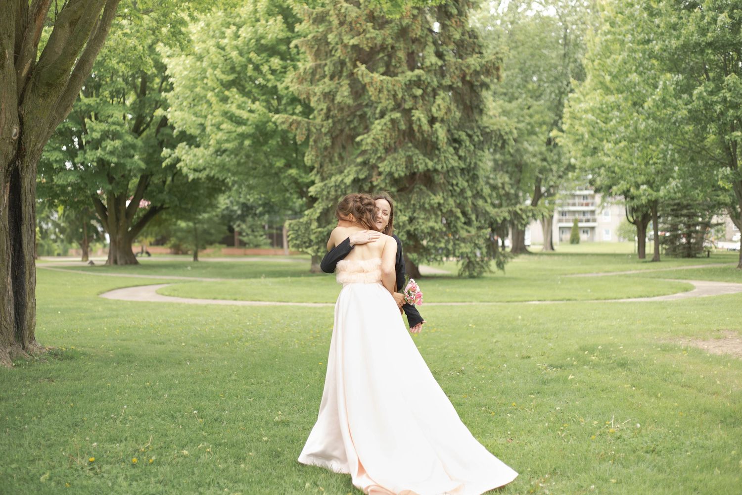 A graceful figure in a flowing white wedding dress twirls in a lush green park setting.