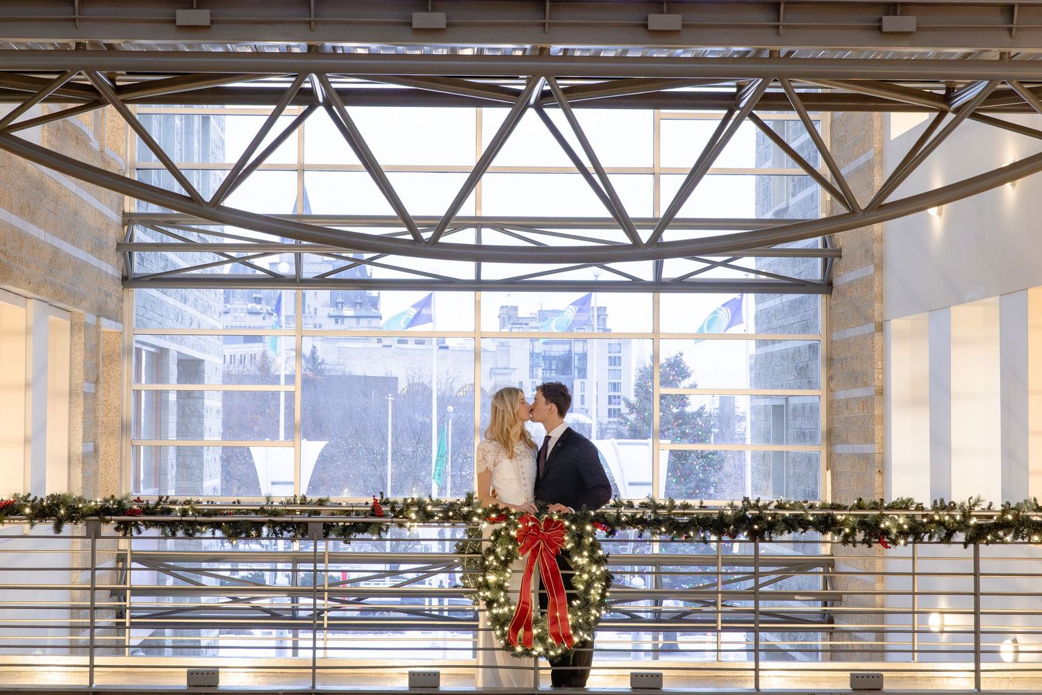 Bright modern office space with large windows, exposed ceiling beams, and festive holiday garland decorations.