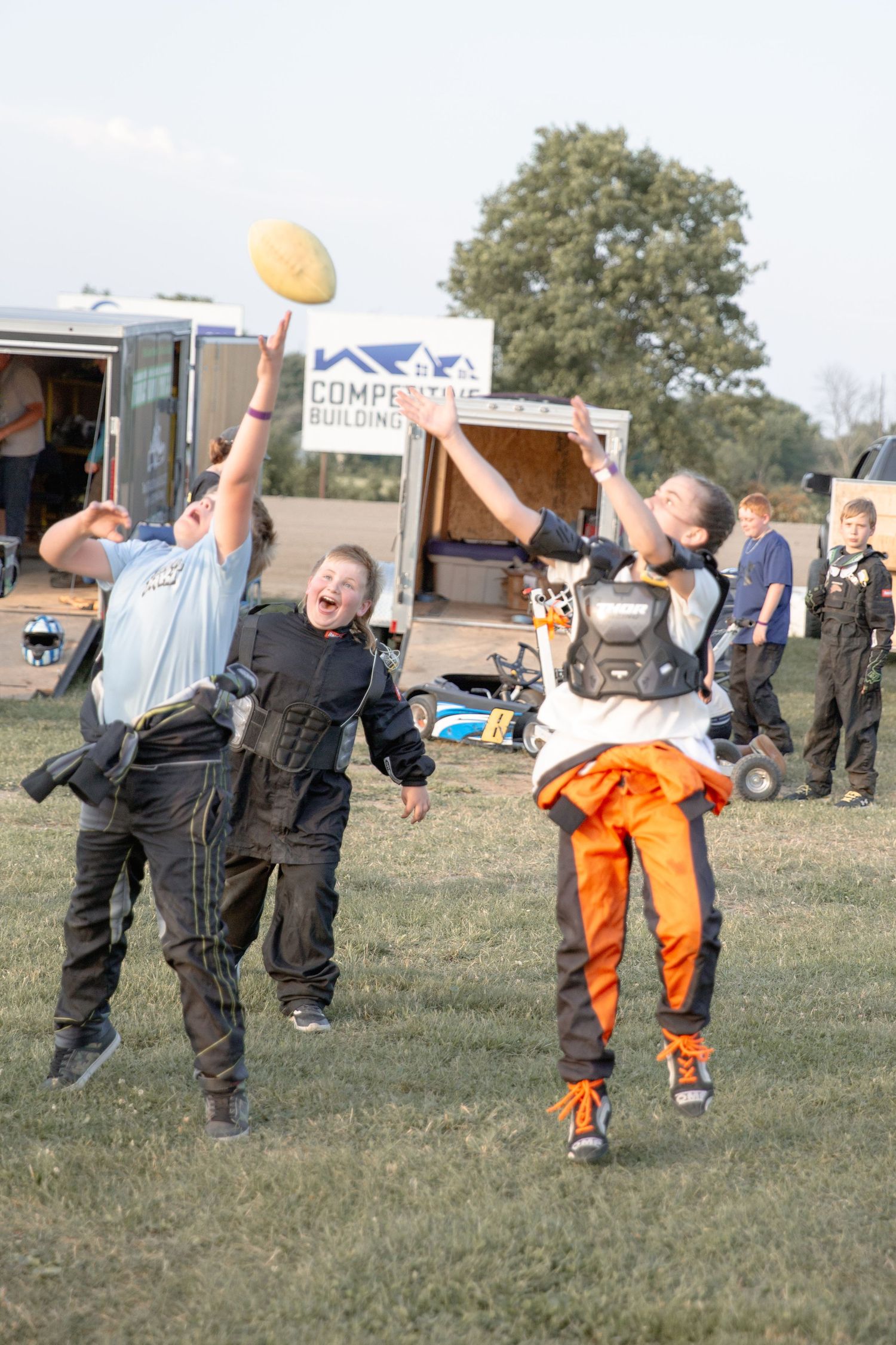 Multiple people toss small yellow balls together in a grassy outdoor field during a group activity.