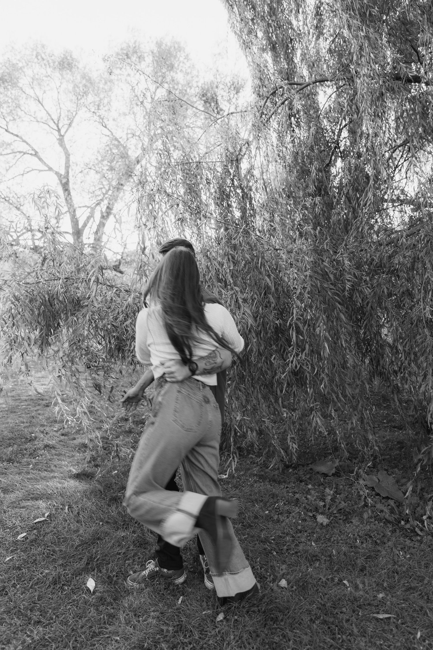 A romantic moment captured in black and white among willow trees and natural foliage.