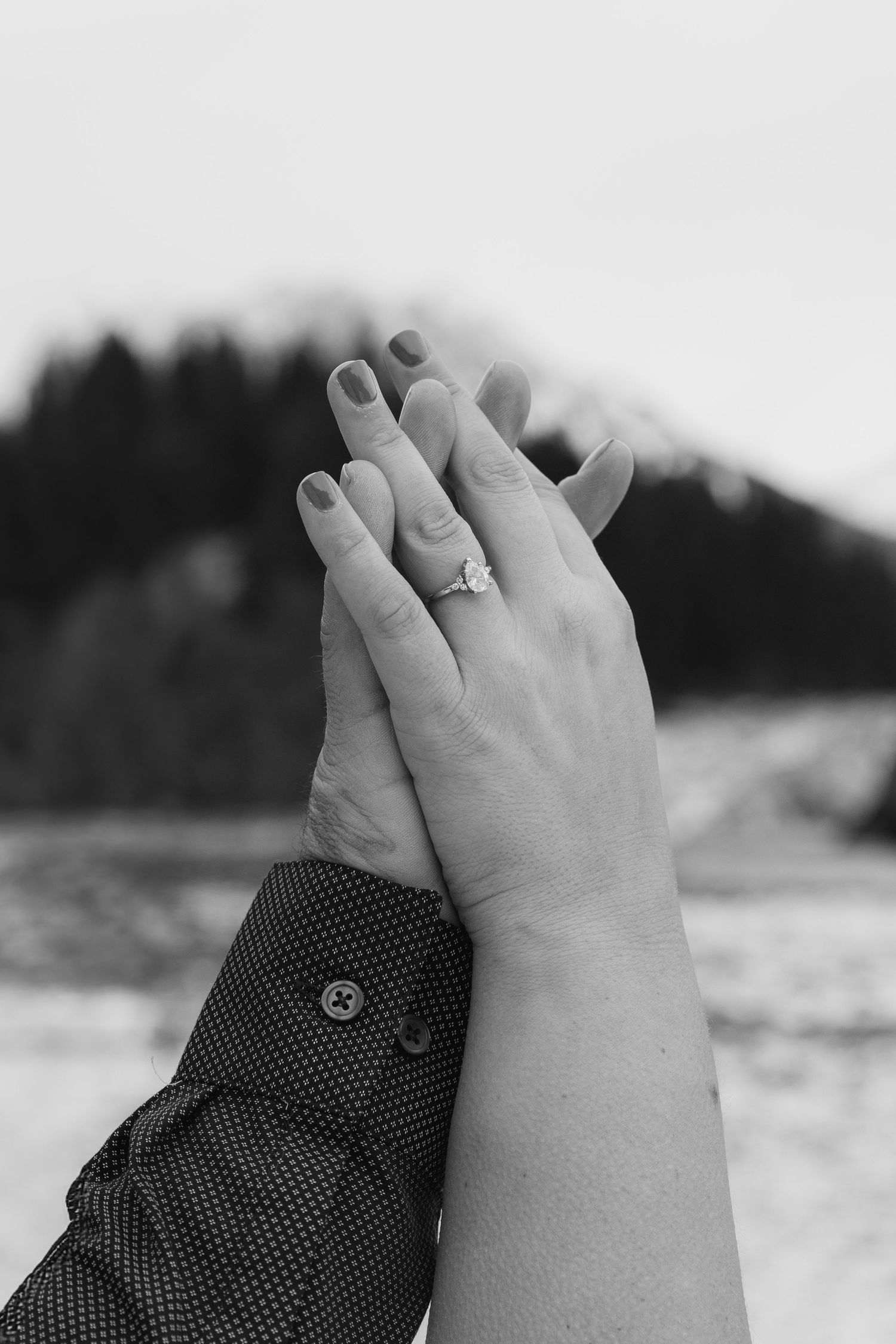 Black and white close-up photo of hands with a ring against a blurred outdoor background.
