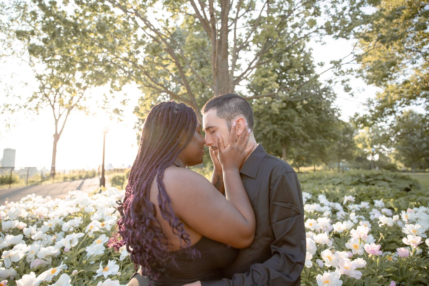 Romantic couple shares tender moments in a sunlit meadow with white flowers during golden hour photography session.